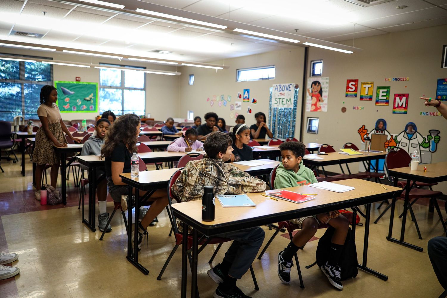 Students sit at desks in a STEM classroom, engaged in learning activities with colorful materials and educational posters on the walls.