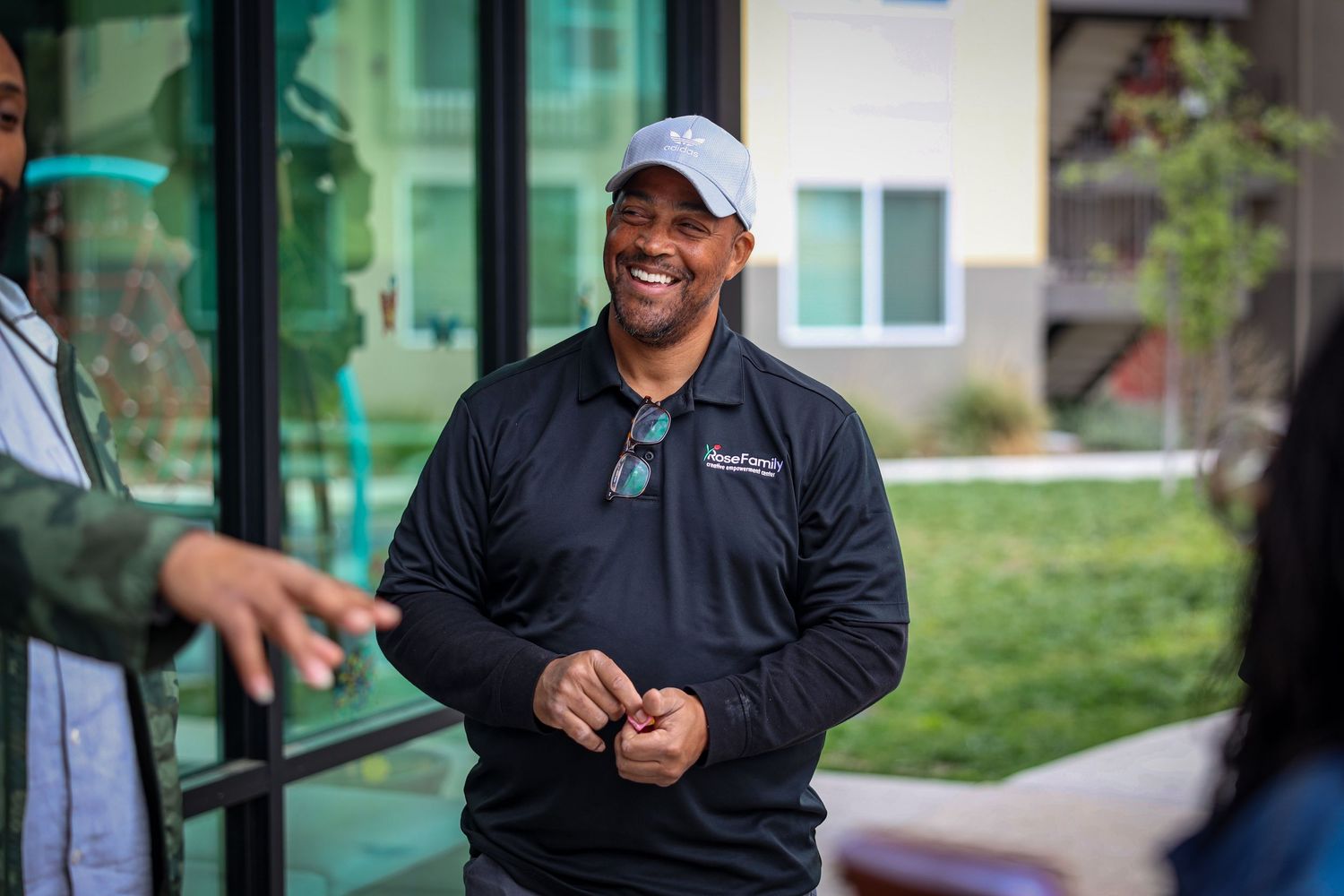 Someone in a black quarter-zip pullover and baseball cap smiles while engaging in conversation outdoors.