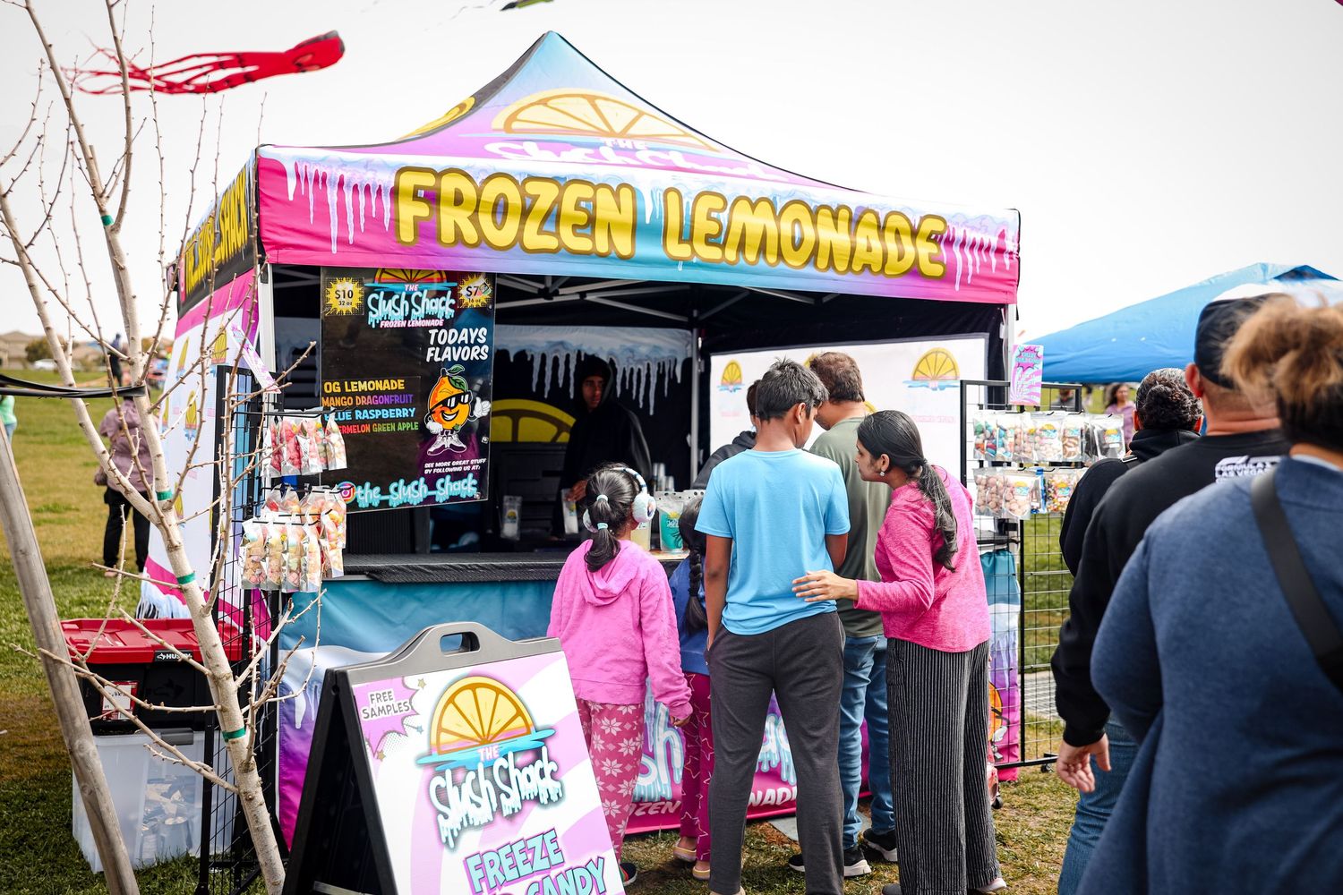 Food carts and vendors serve customers at an outdoor festival with colorful tents and signage.