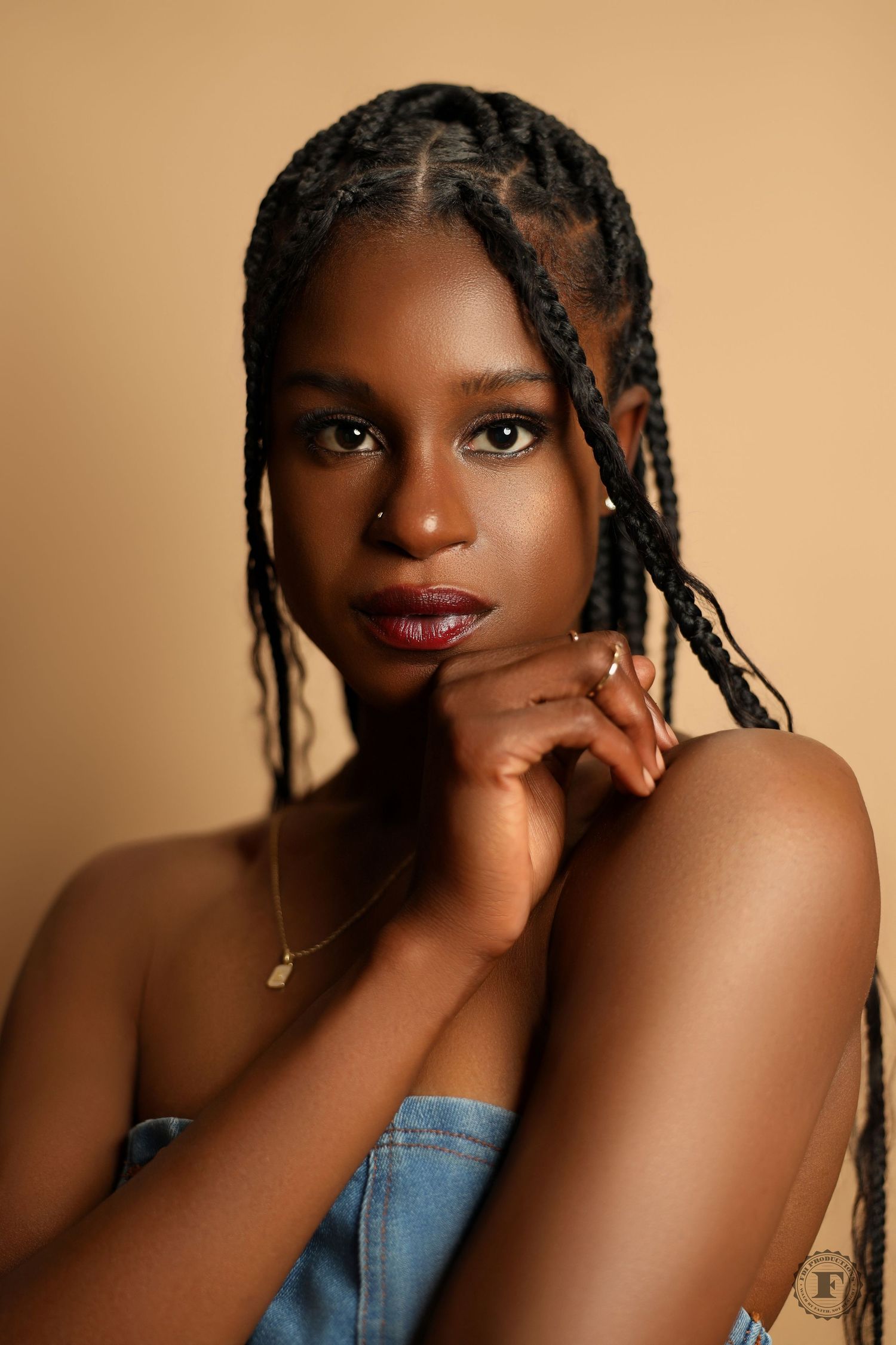 Beautiful studio portrait with braided hairstyle against warm brown backdrop wearing denim, lit with soft natural lighting.