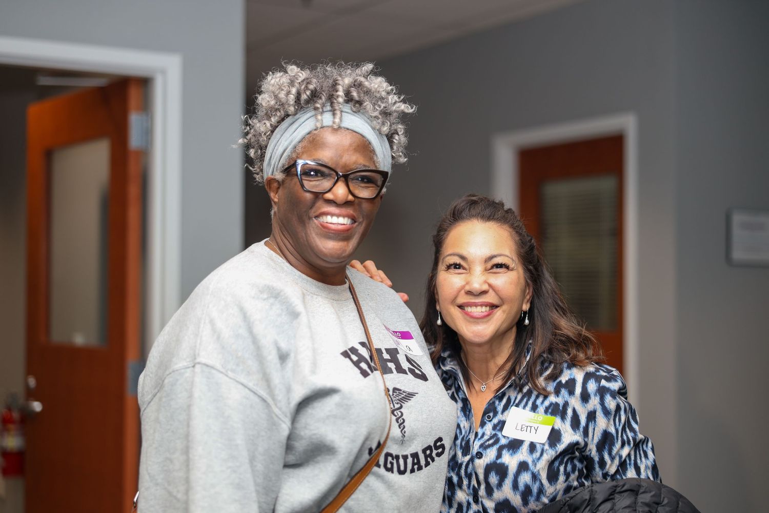 Two women smiling and posing together indoors, one wearing a gray Jaguars sweatshirt and glasses.