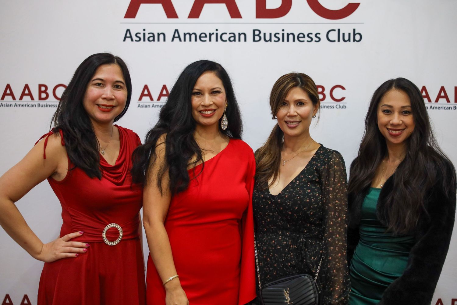 A group of professionally dressed women in red and dark colored outfits pose together at an Asian American Business Club event.