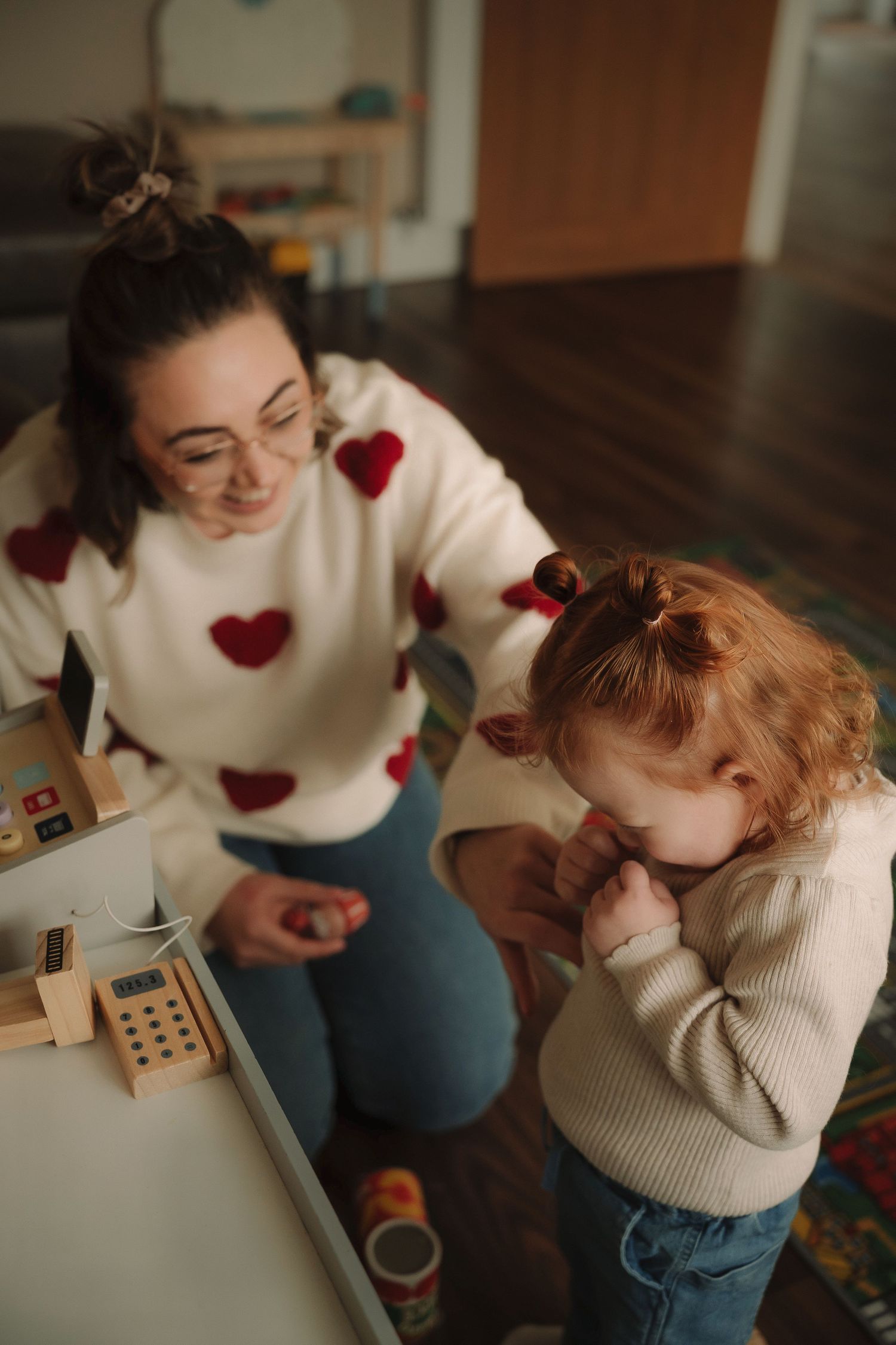 A series of candid moments showing someone wearing a white sweater with red hearts sitting and reading on a wooden floor.