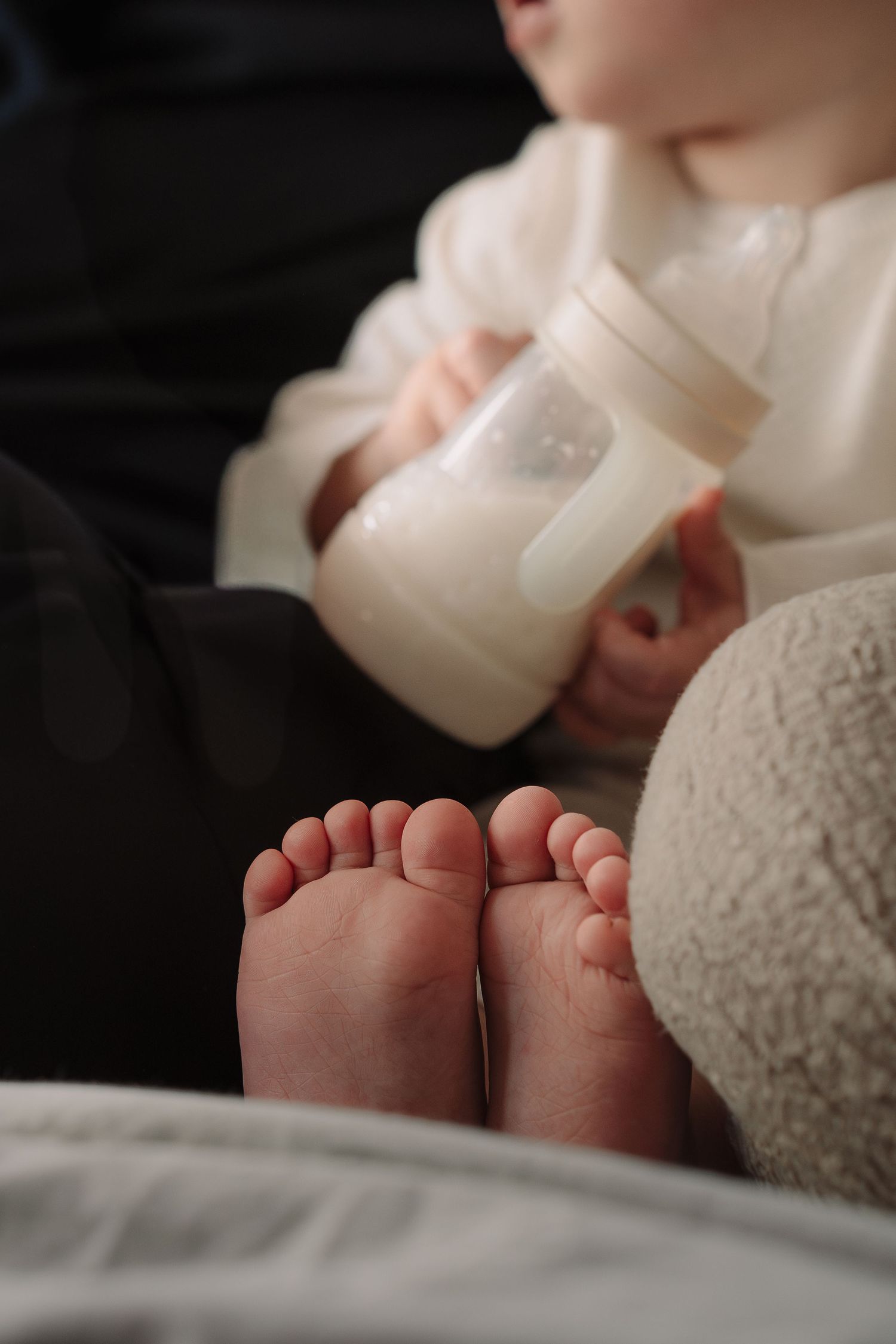 Close-up of a baby's tiny feet while holding a milk bottle in soft natural light.