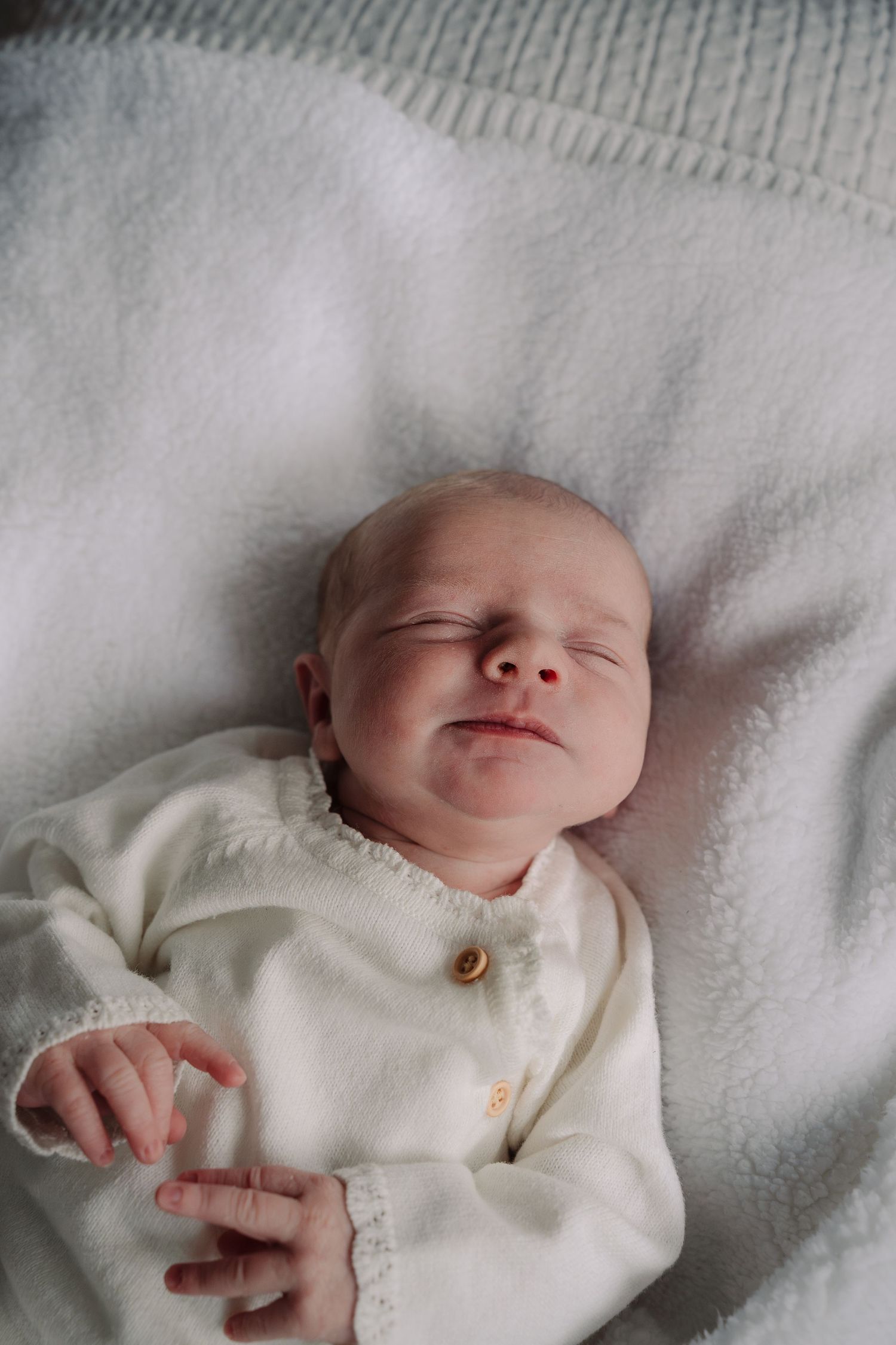 Peaceful newborn baby sleeping in white outfit on soft blanket.