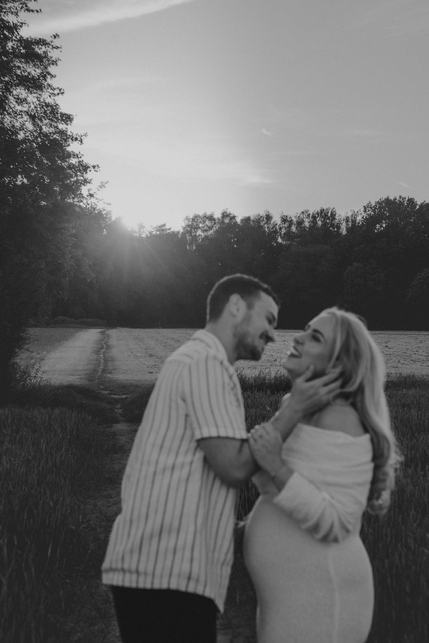 Black and white photo of a couple sharing a romantic moment in a field at sunset, man tenderly holding womans face.