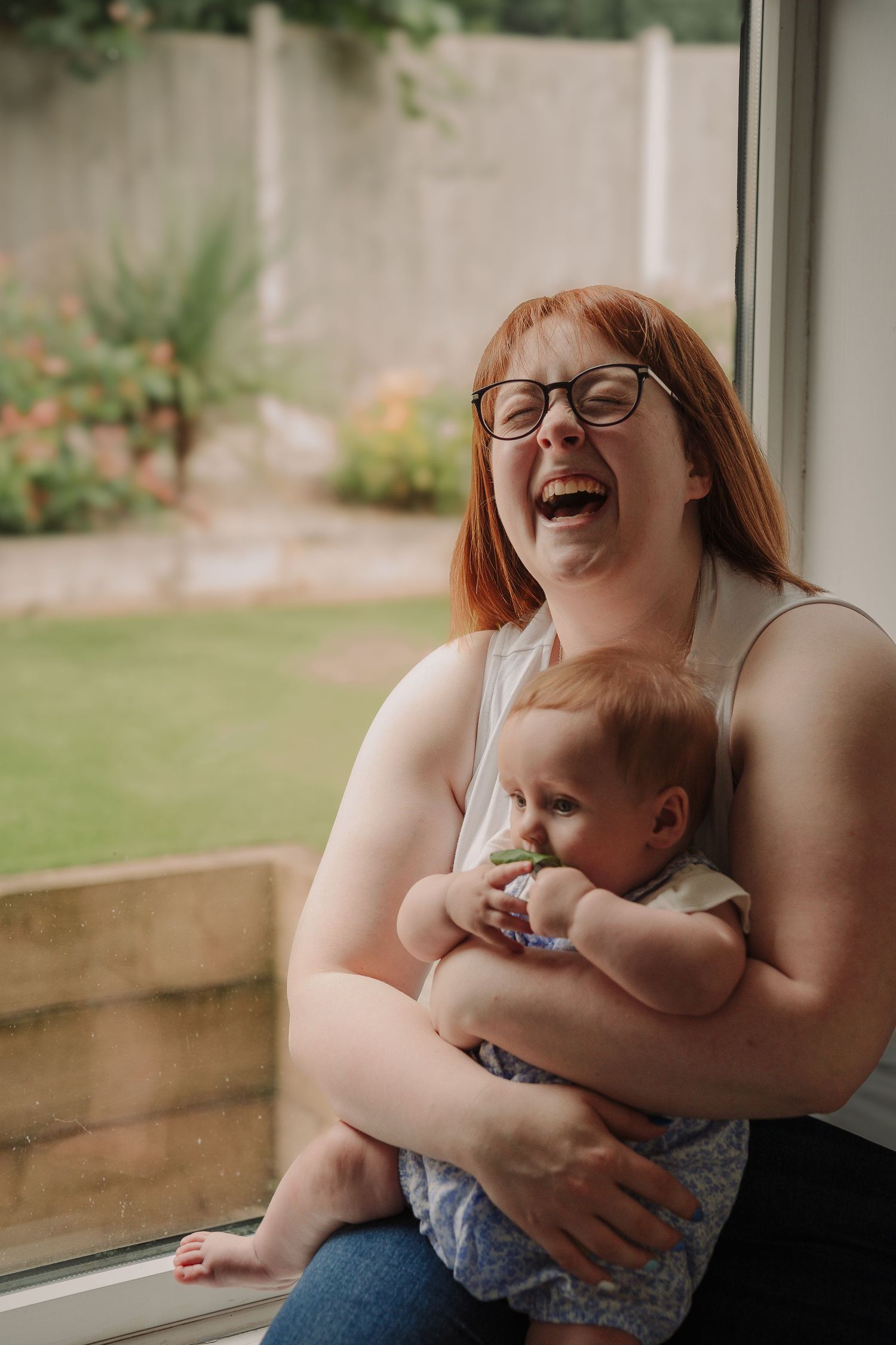 A joyful moment shared between parent and baby sitting by a window with natural light streaming in.