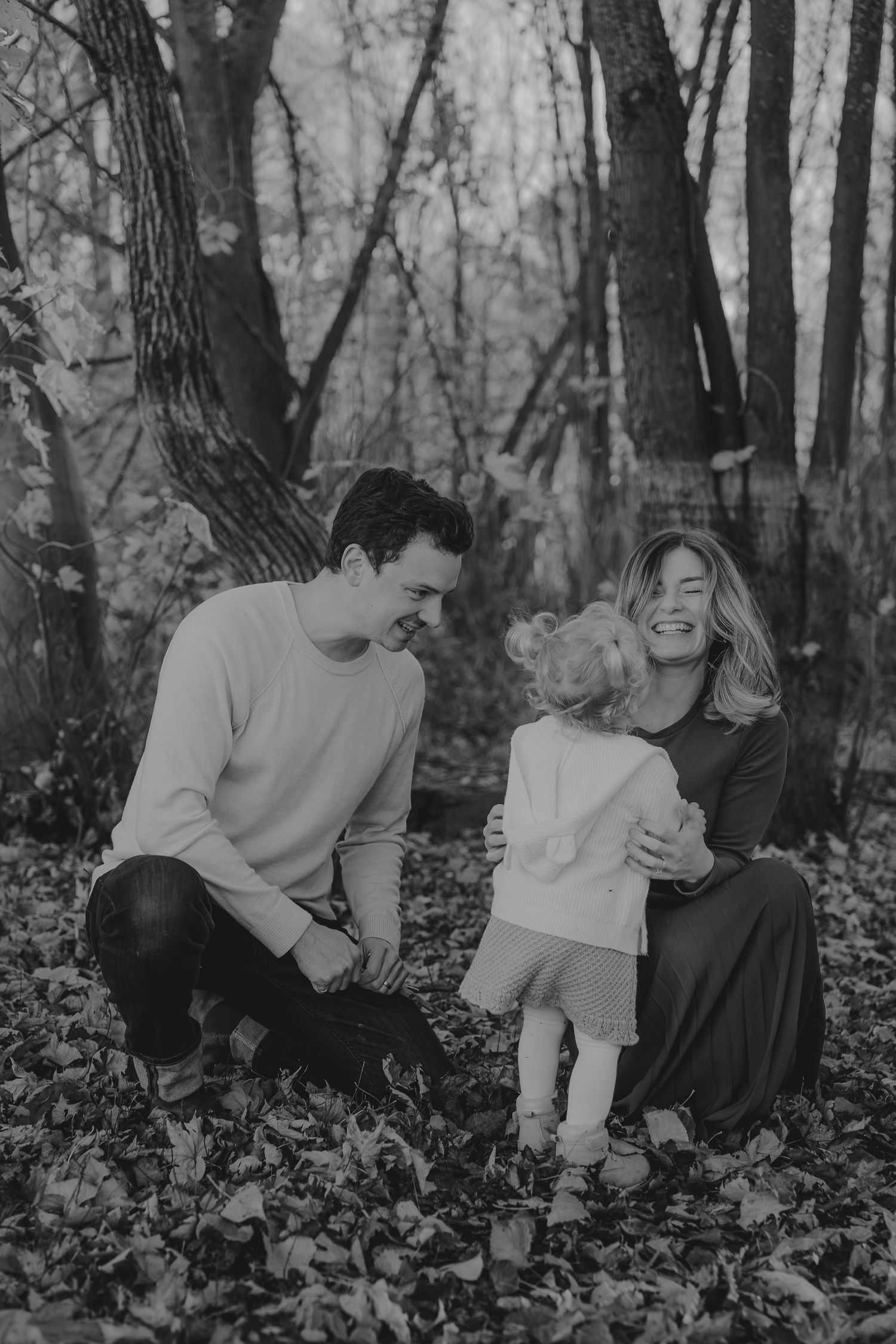 Black and white family photo session in a wooded setting with fallen leaves.