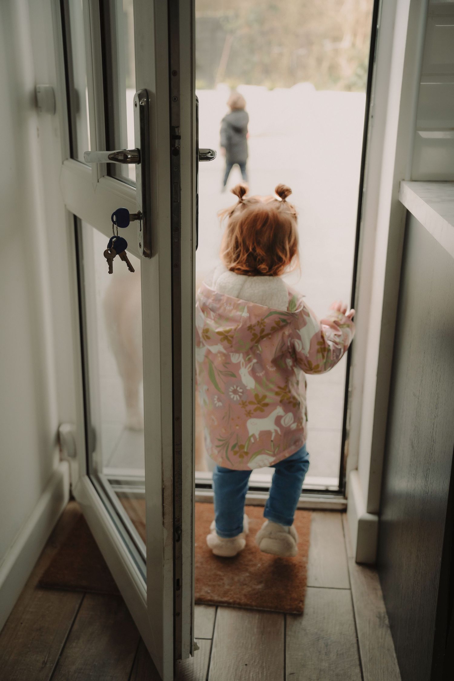 A child in a pink sweater and jeans peers out through a glass door in a sequence of four similar photos.