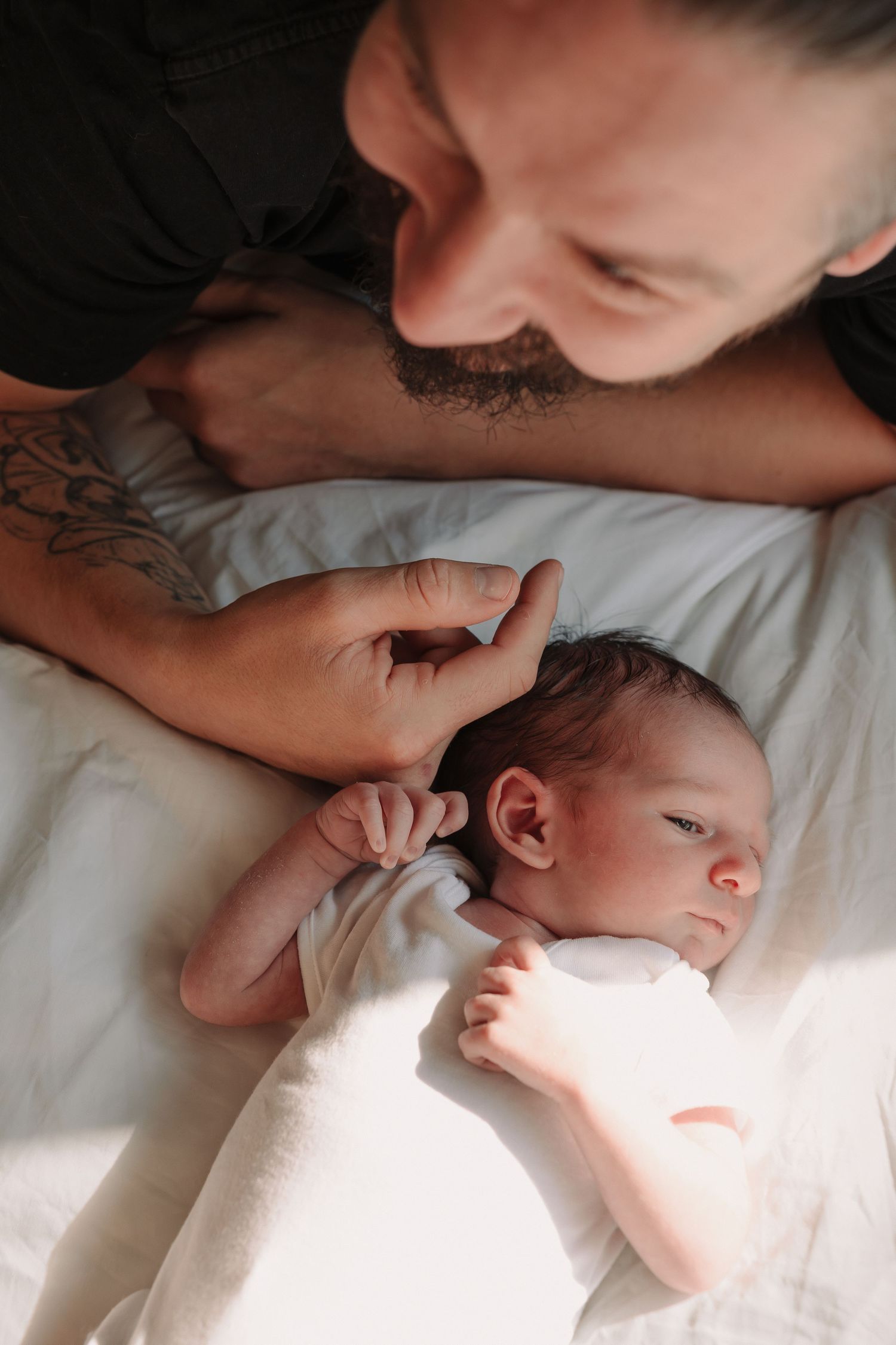 A parent leans down to give a gentle kiss to a sleeping baby wrapped in white bedding.
