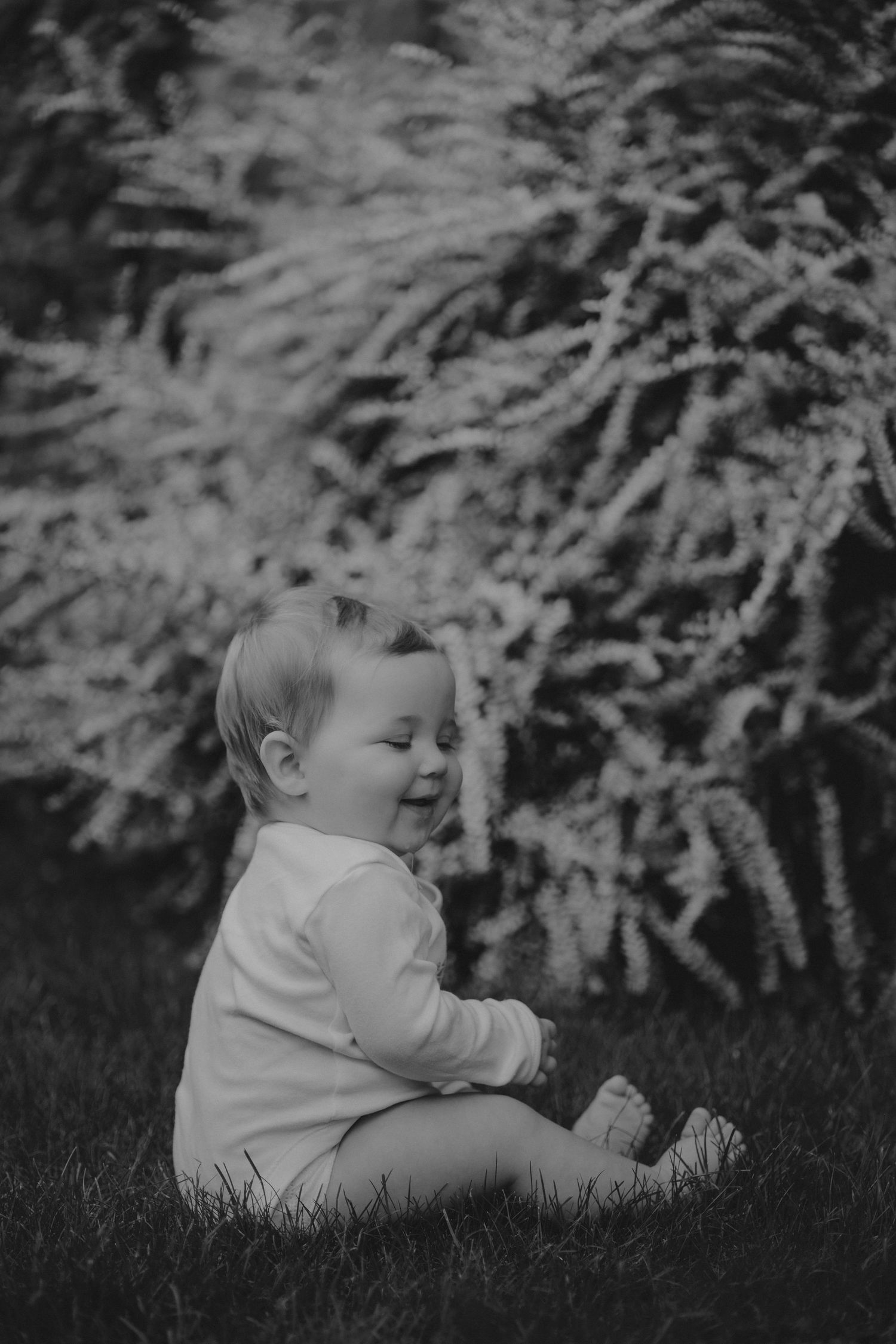 black and white image of baby sitting in the grass laughing by a Tamworth milestone photographer.