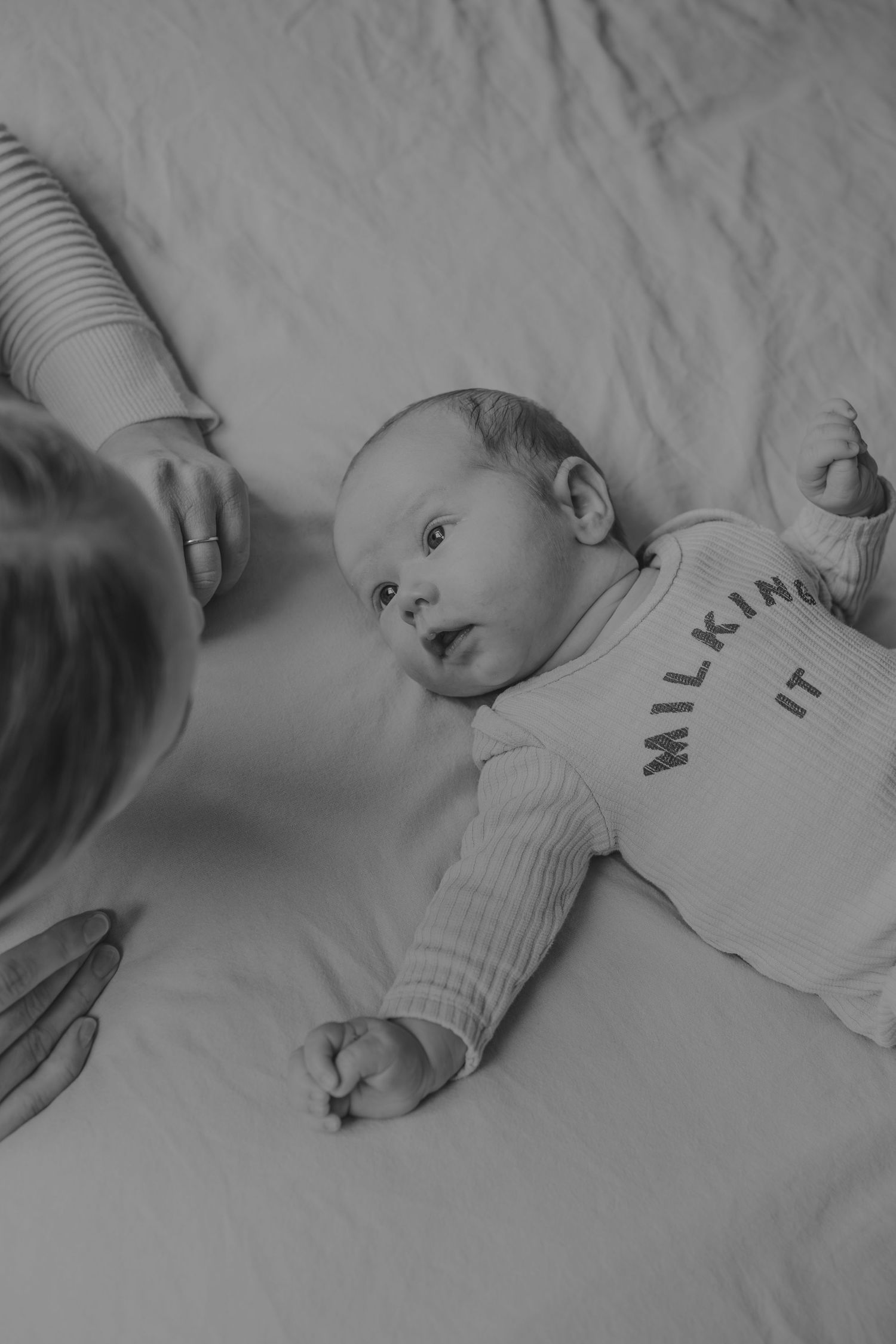 A black and white series of photos showing a baby lying on white bedding wearing a light colored onesie.