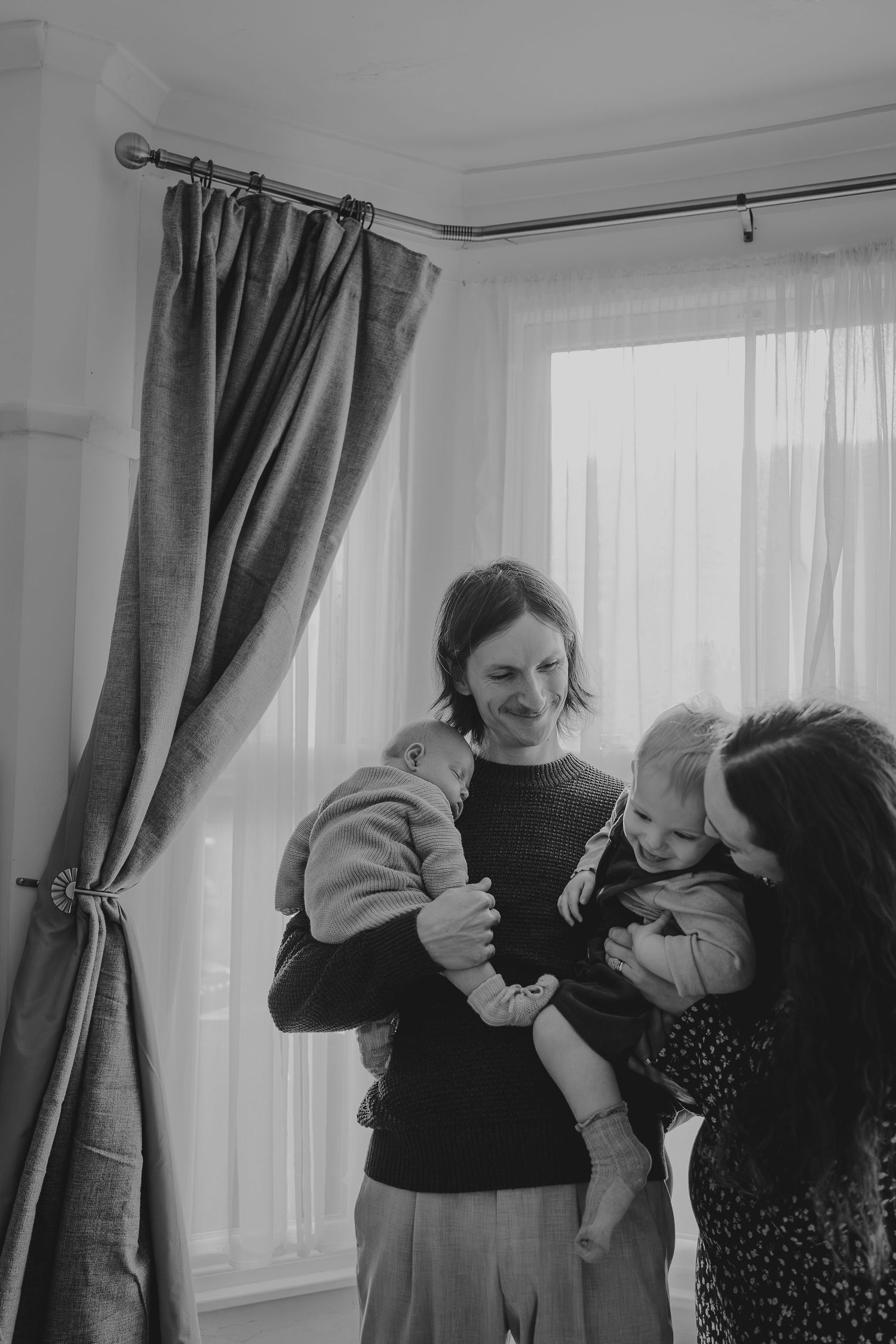 A series of candid moments showing playful interaction between adult and infant by a curtained window.