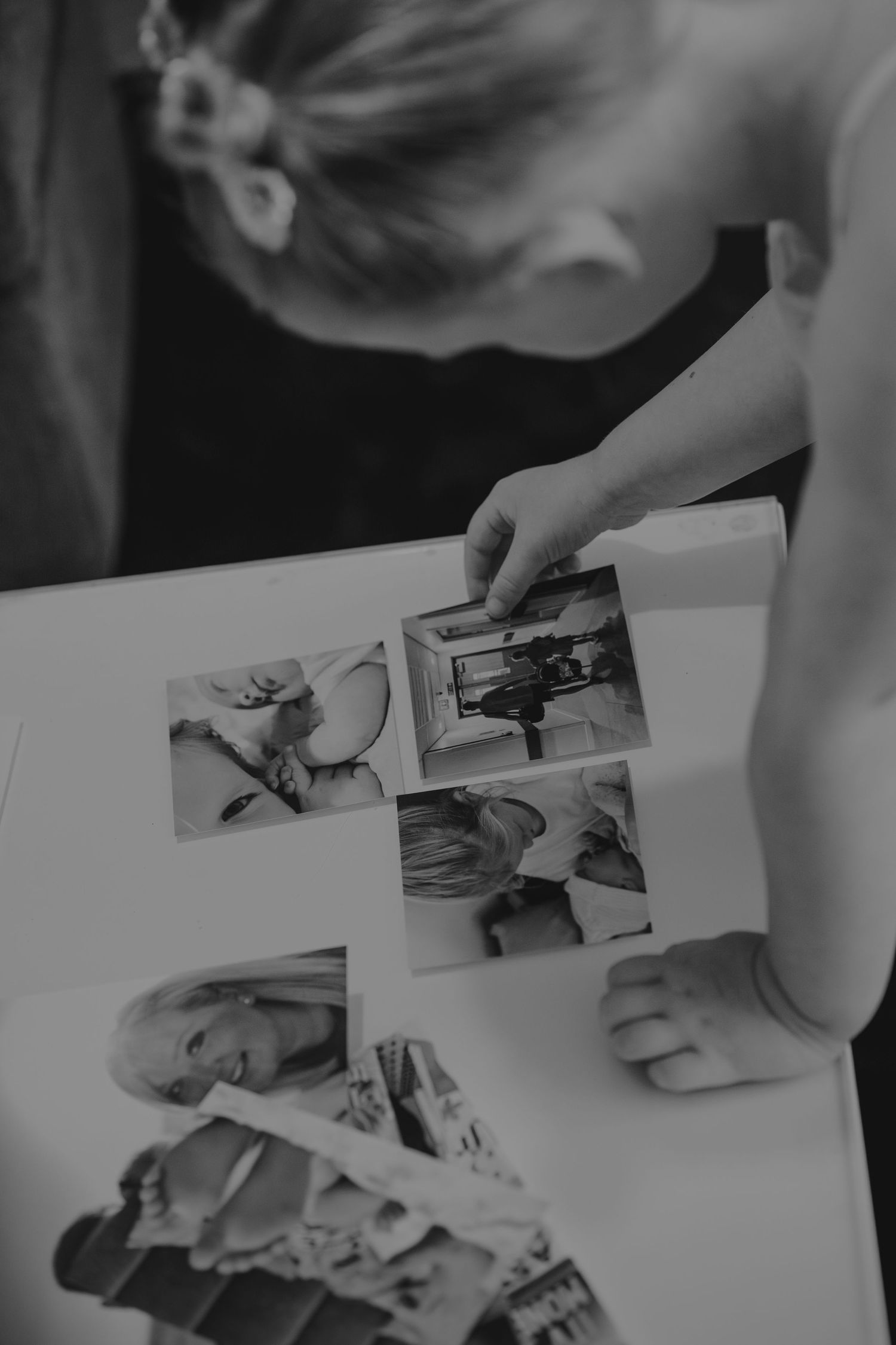 Hands arranging black and white photographs on a light surface.
