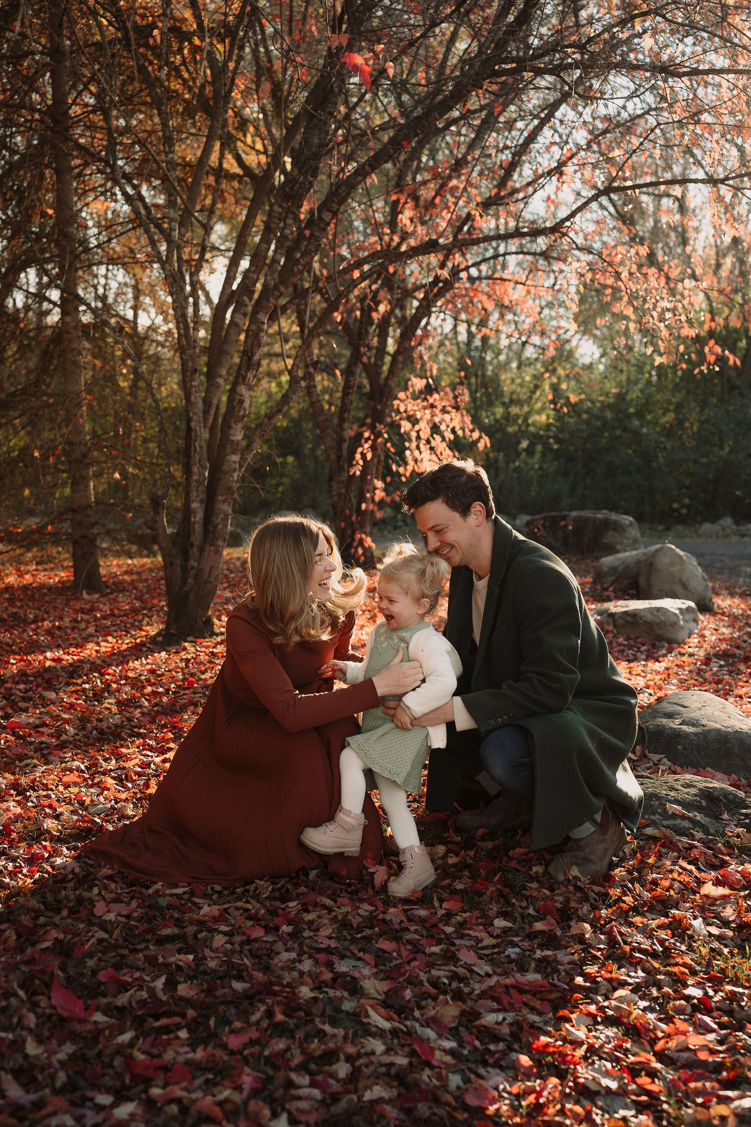 Family lying on autumn leaves having a candid moment together in warm sunset light.