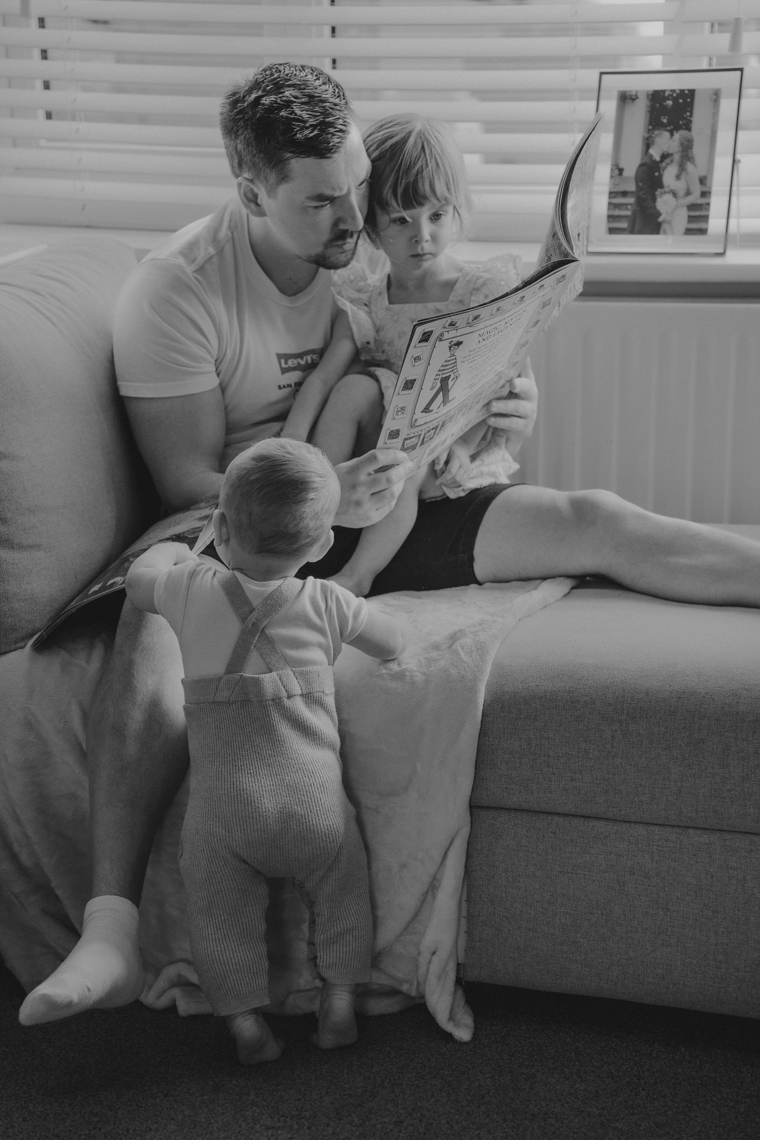 A family sits together on a couch reading a book in a series of black and white photographs.