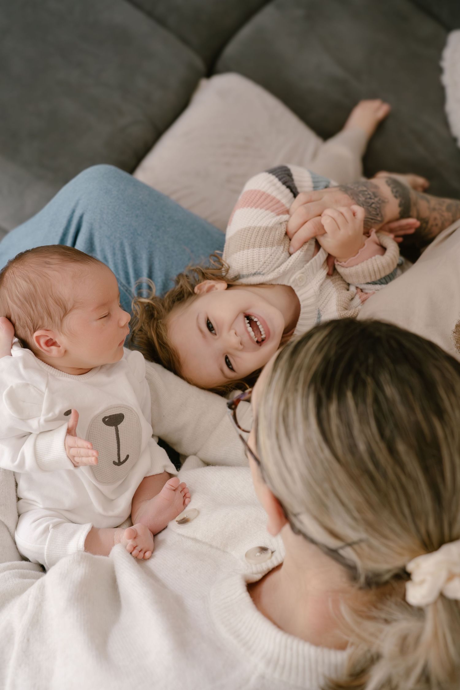 A parent and child share joyful moments together while lying on a bed in matching white sweaters.