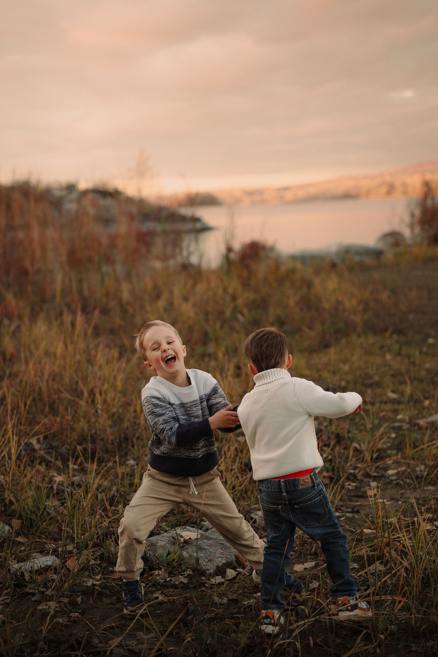 Two young children playing and running together in a field during golden hour by Tamworth family photographer.
