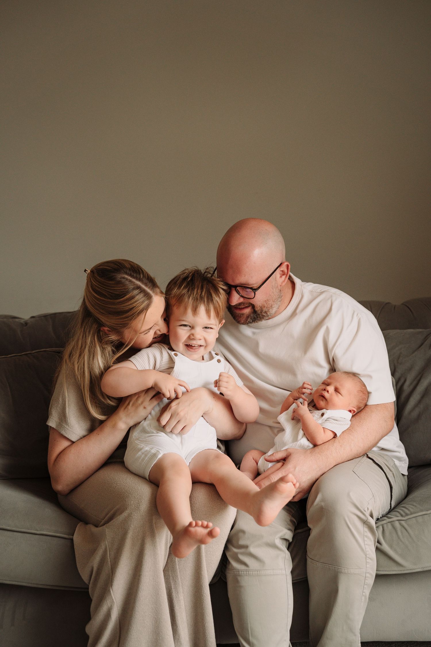 Family lounging together on a gray couch sharing playful moments.