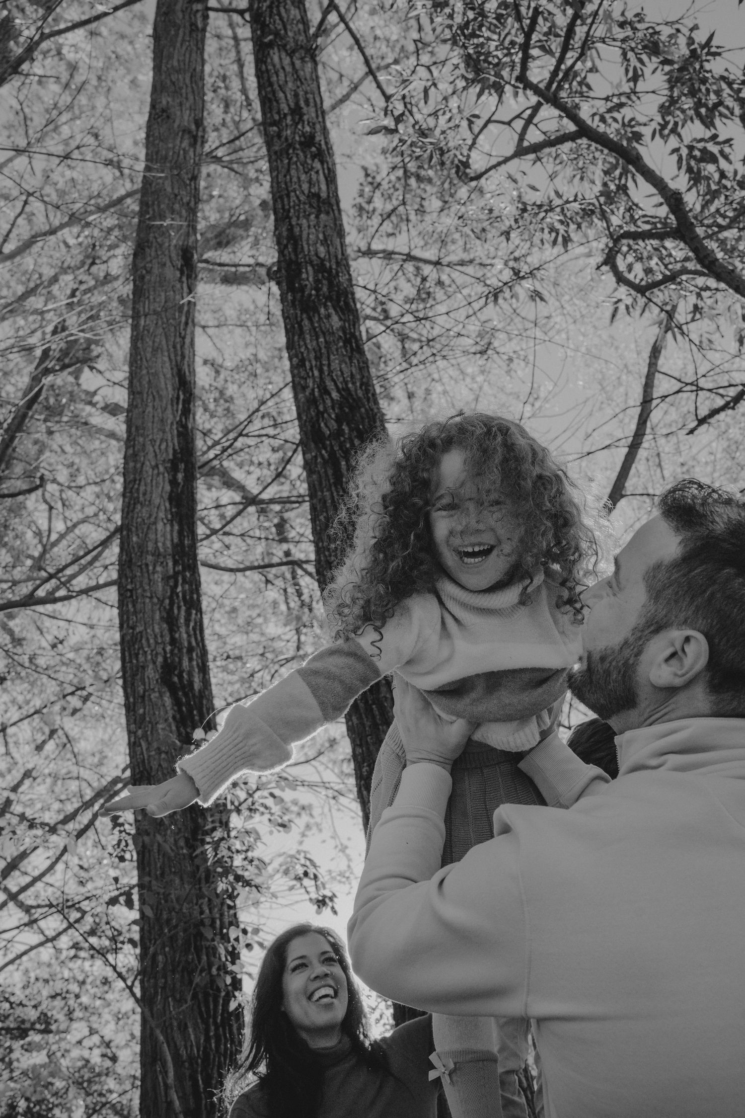 Black and white photo of joyful family moment outdoors among trees.