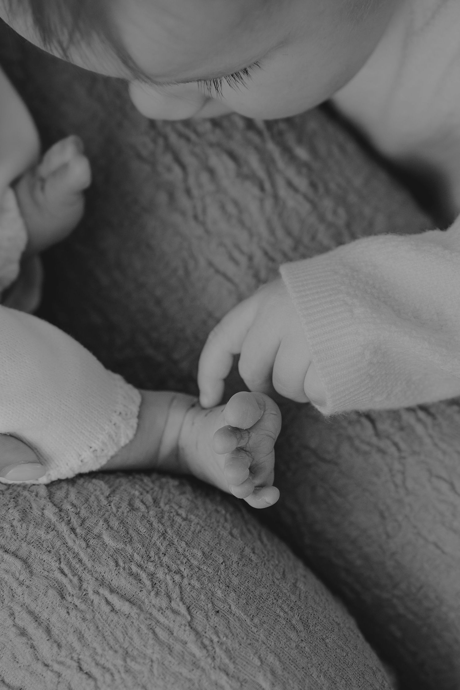 Black and white photo of a toddler gently holding a newborn baby's tiny hand.