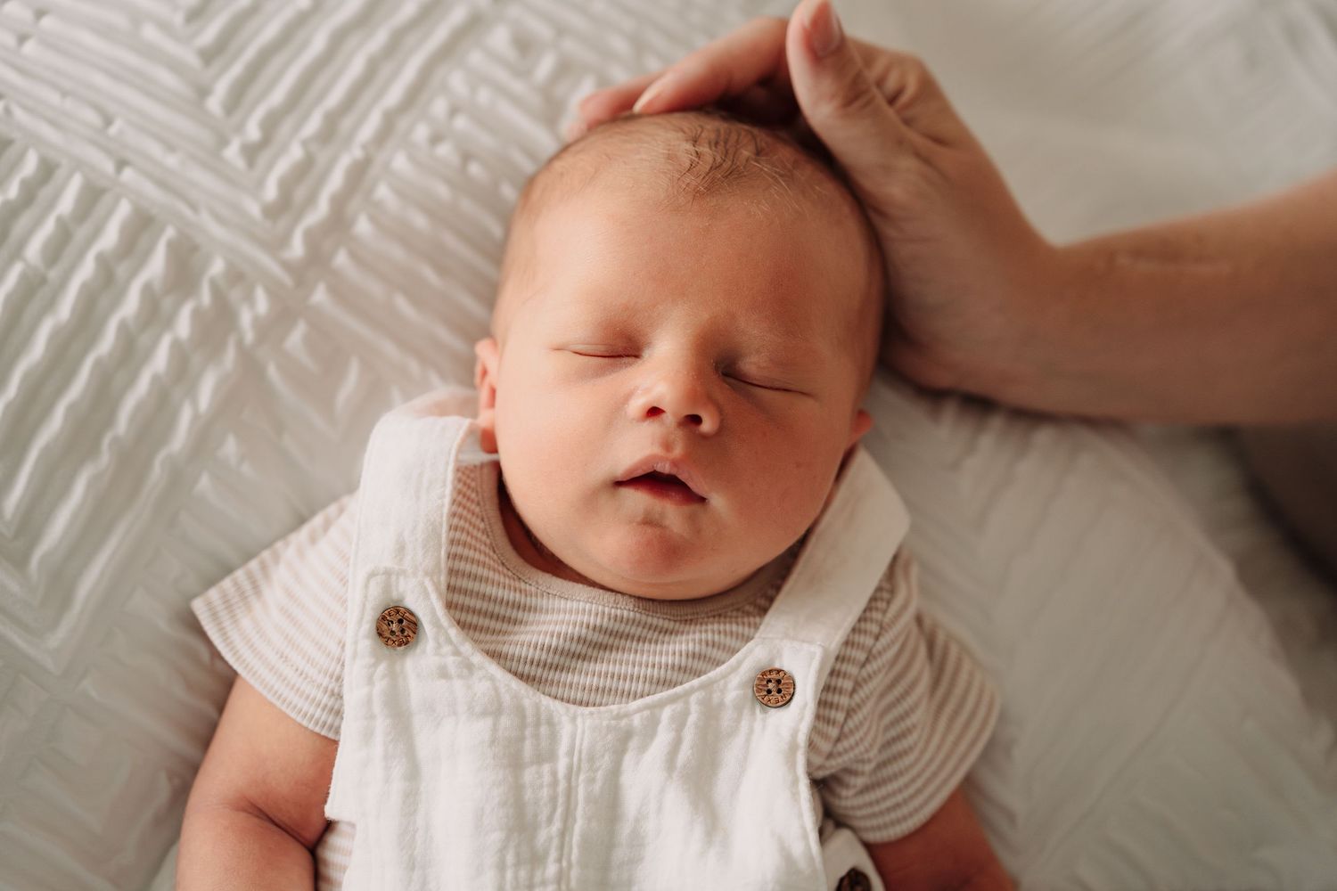 Close-up of baby in white romper on textured bedding.
