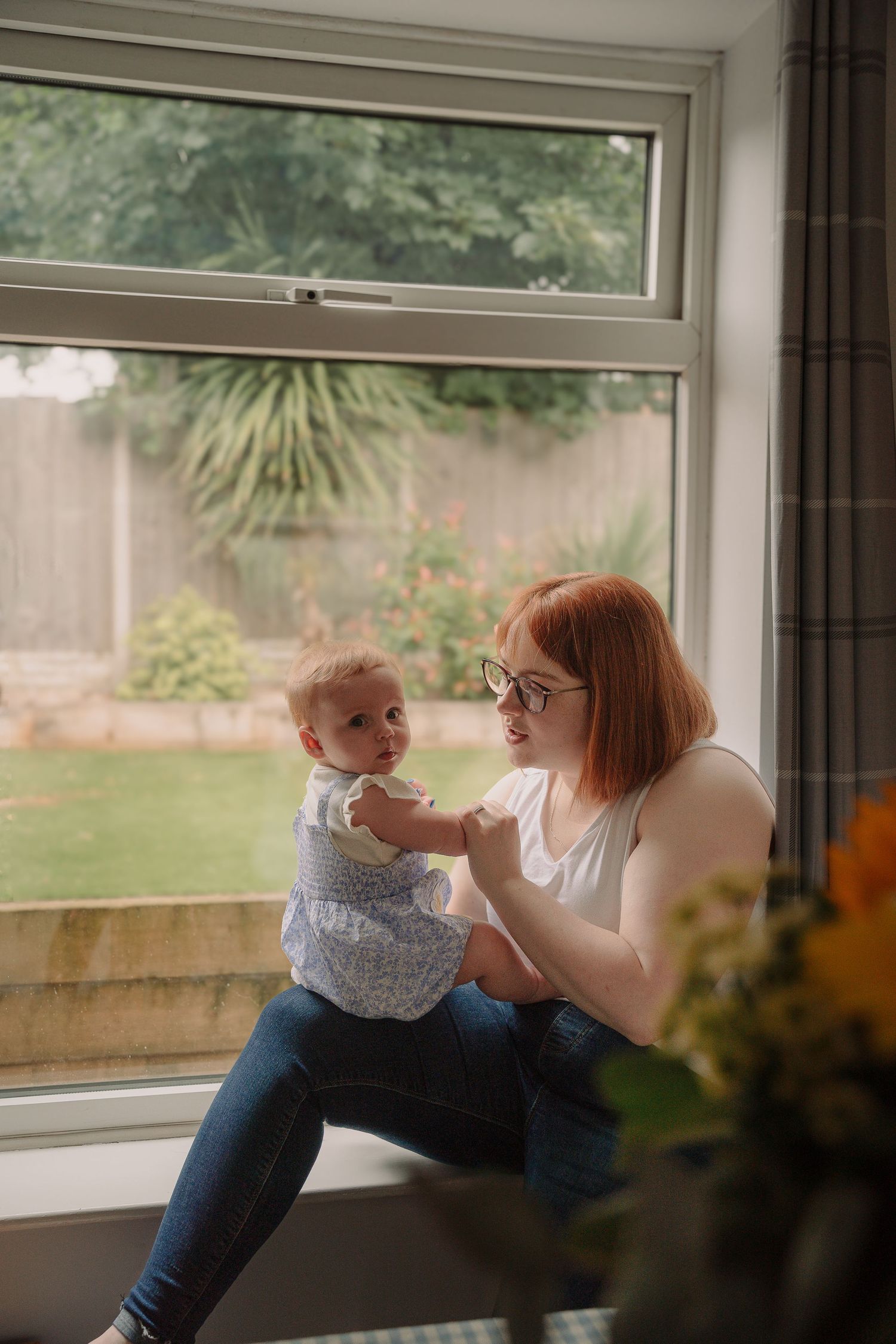 Parent and baby playing together on a window seat with greenery visible outside.