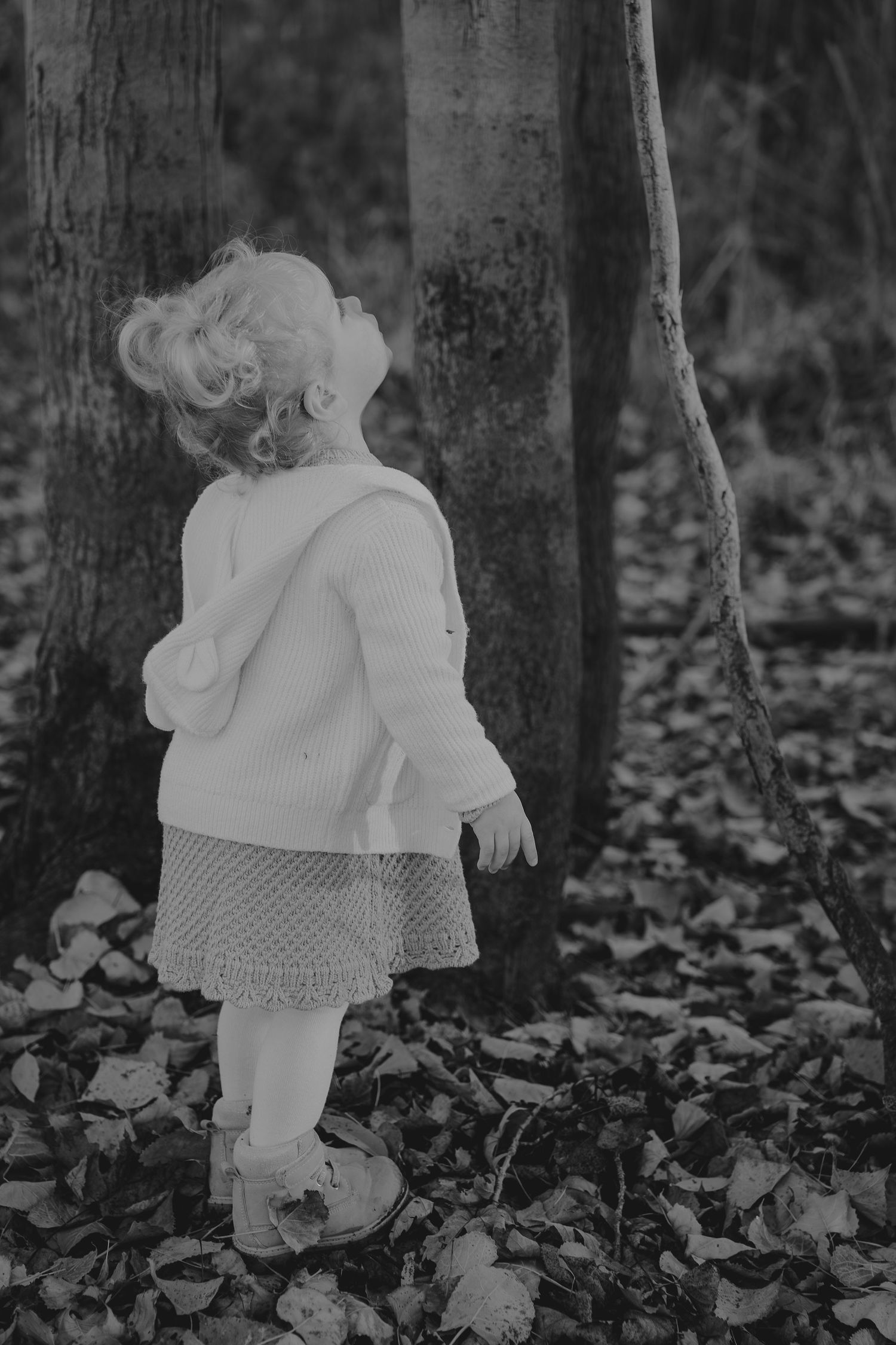 Black and white photos of a small child walking among trees in a white dress.