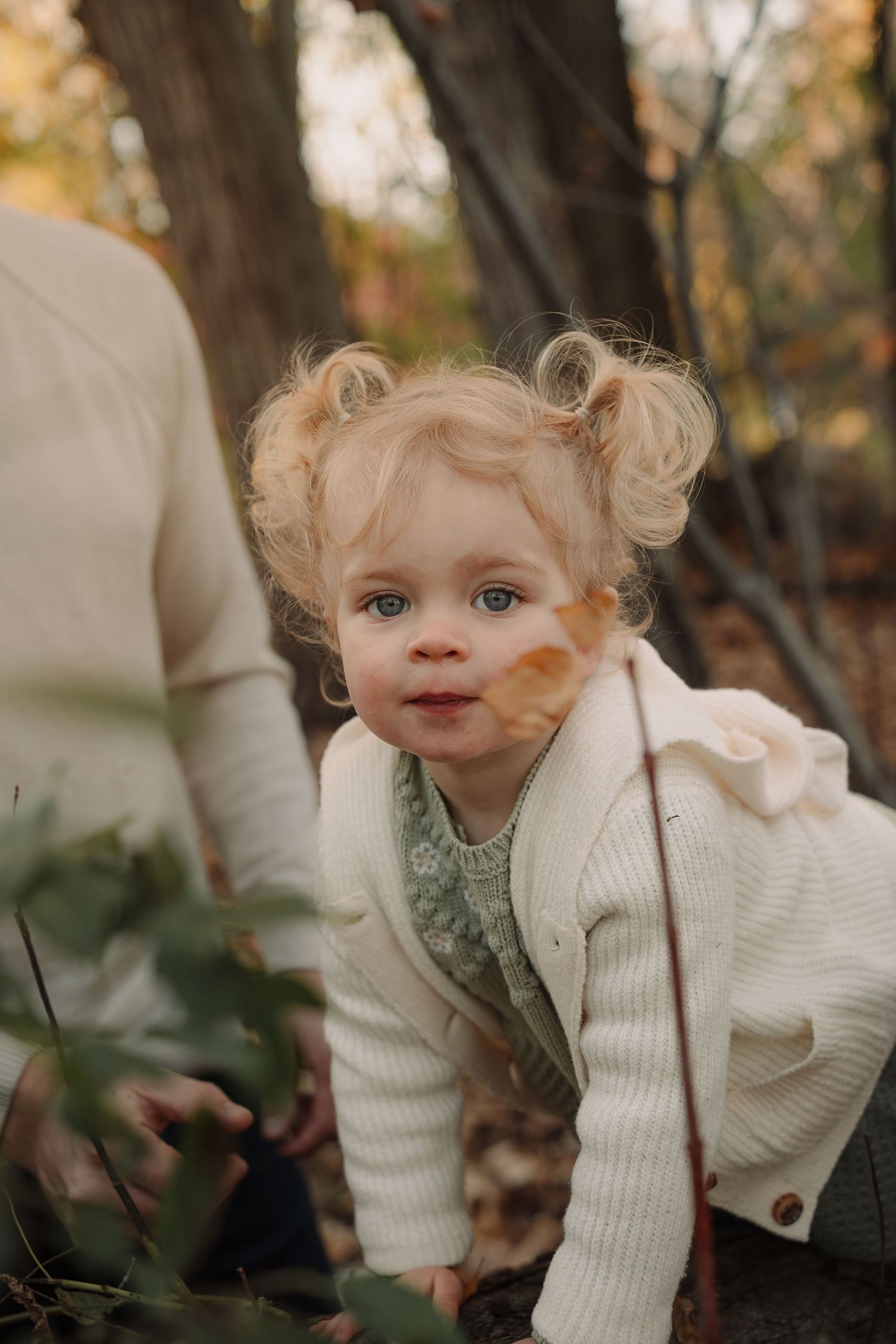 Child in cozy white cardigan explores nature during fall season.