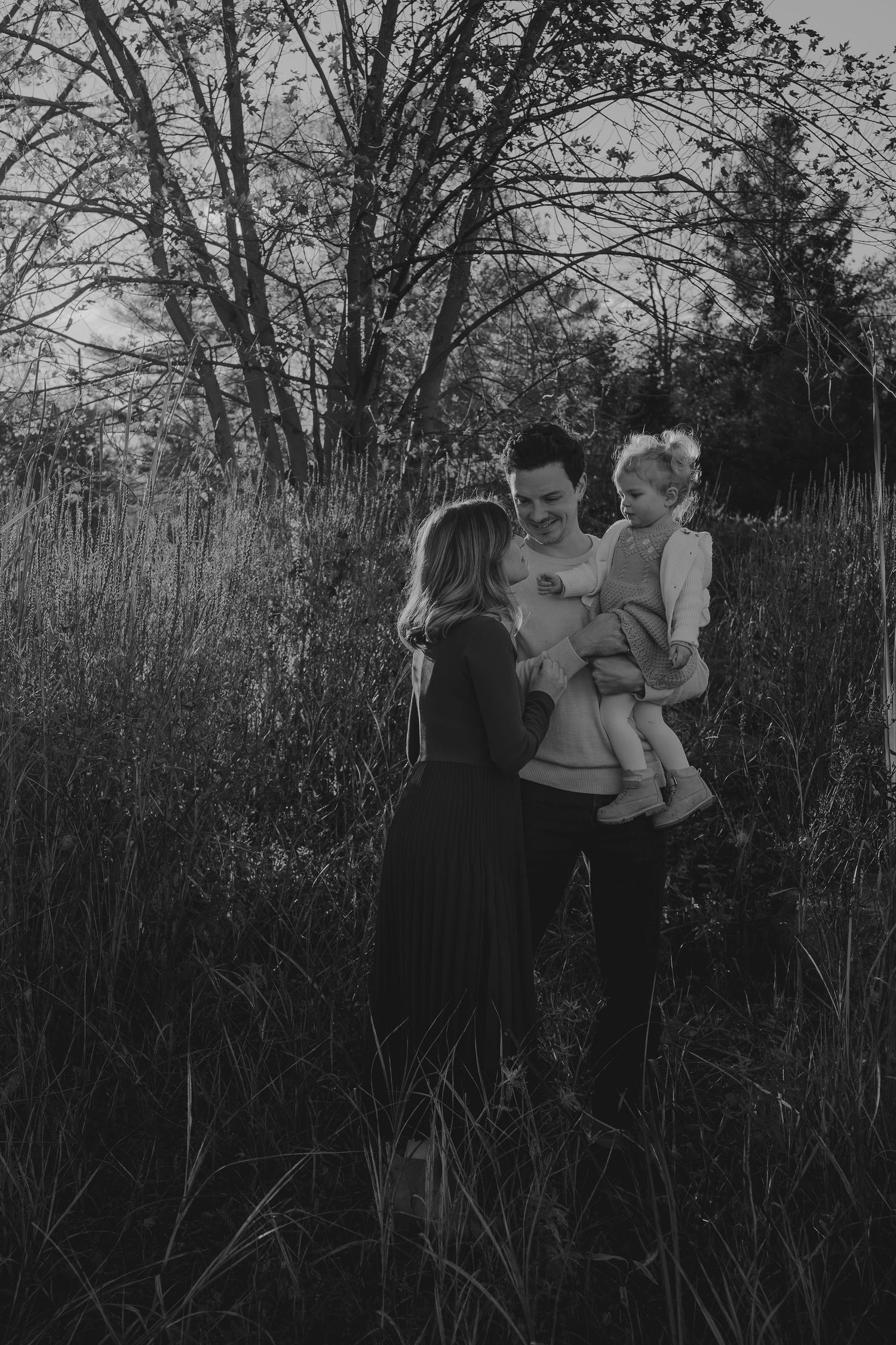 Family portrait session in tall grass and trees during sunset.