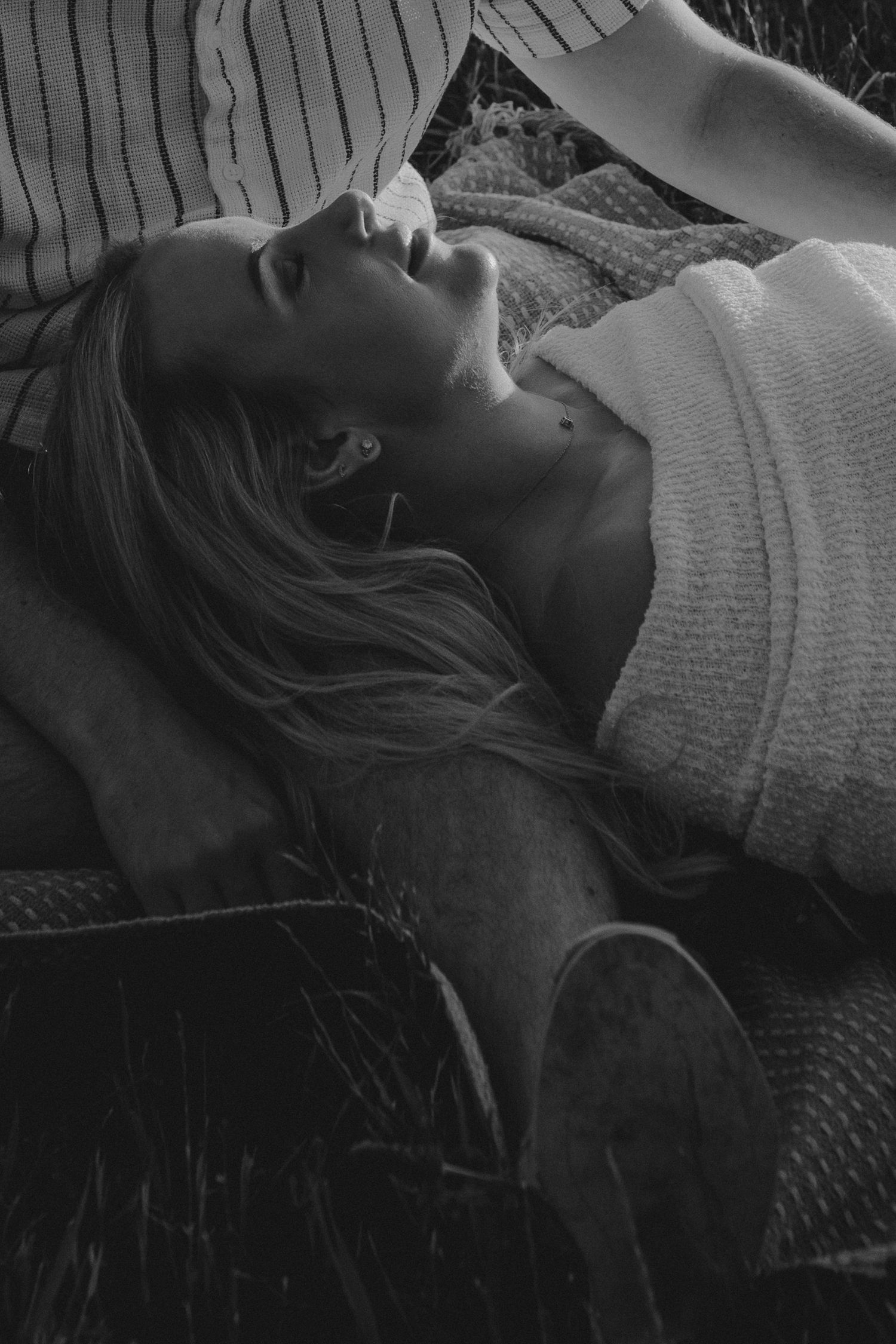 Black and white photo of a young woman lying in grass, gazing upward, wearing a knit sweater.