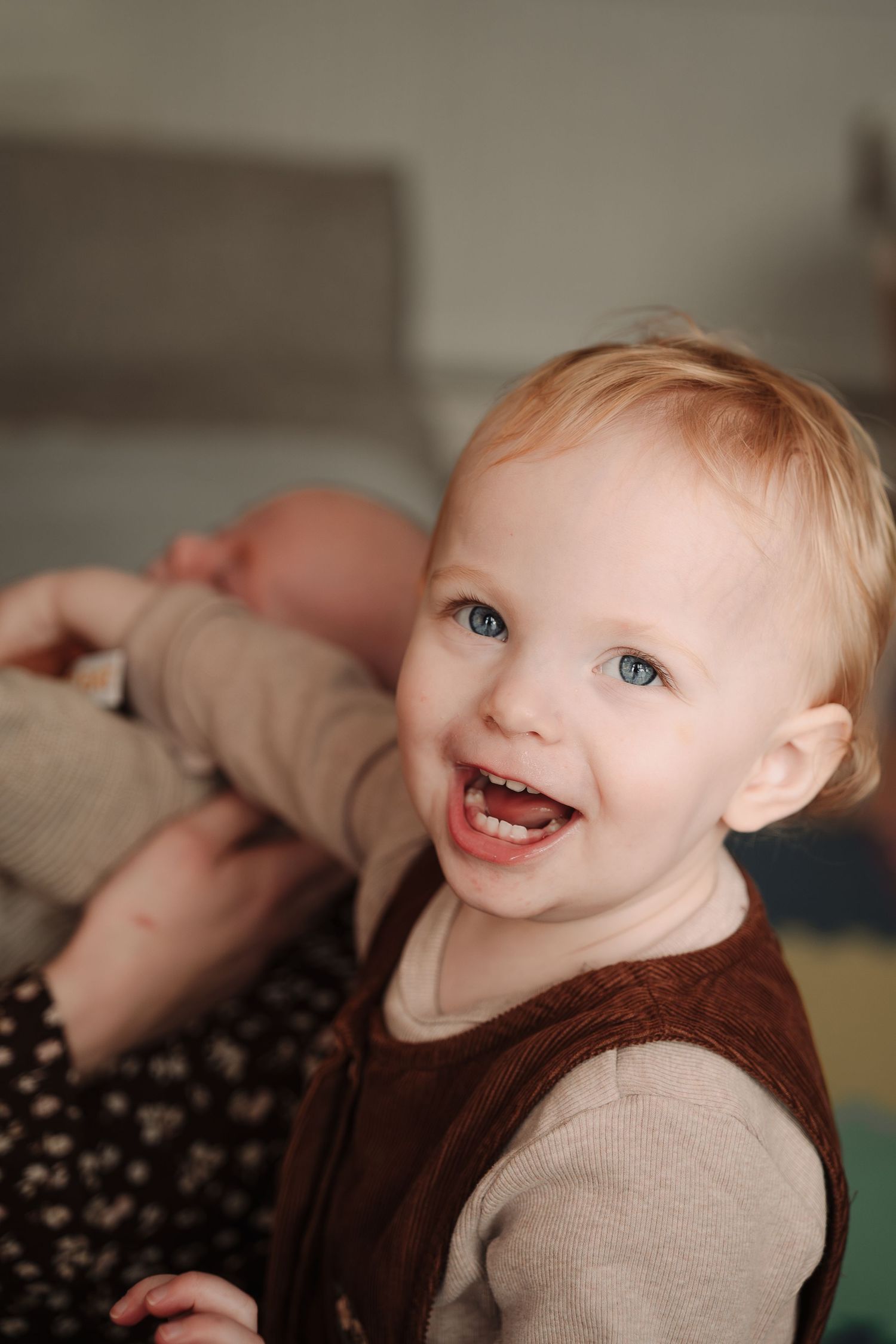 A joyful toddler laughing while wearing a brown and beige sweater.