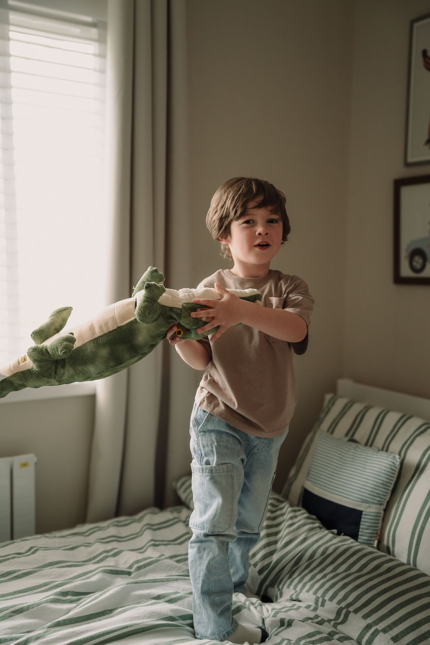 Little boy on his bed swinging around a crocodile soft toy during an at home session by Tamworth newborn photographer.