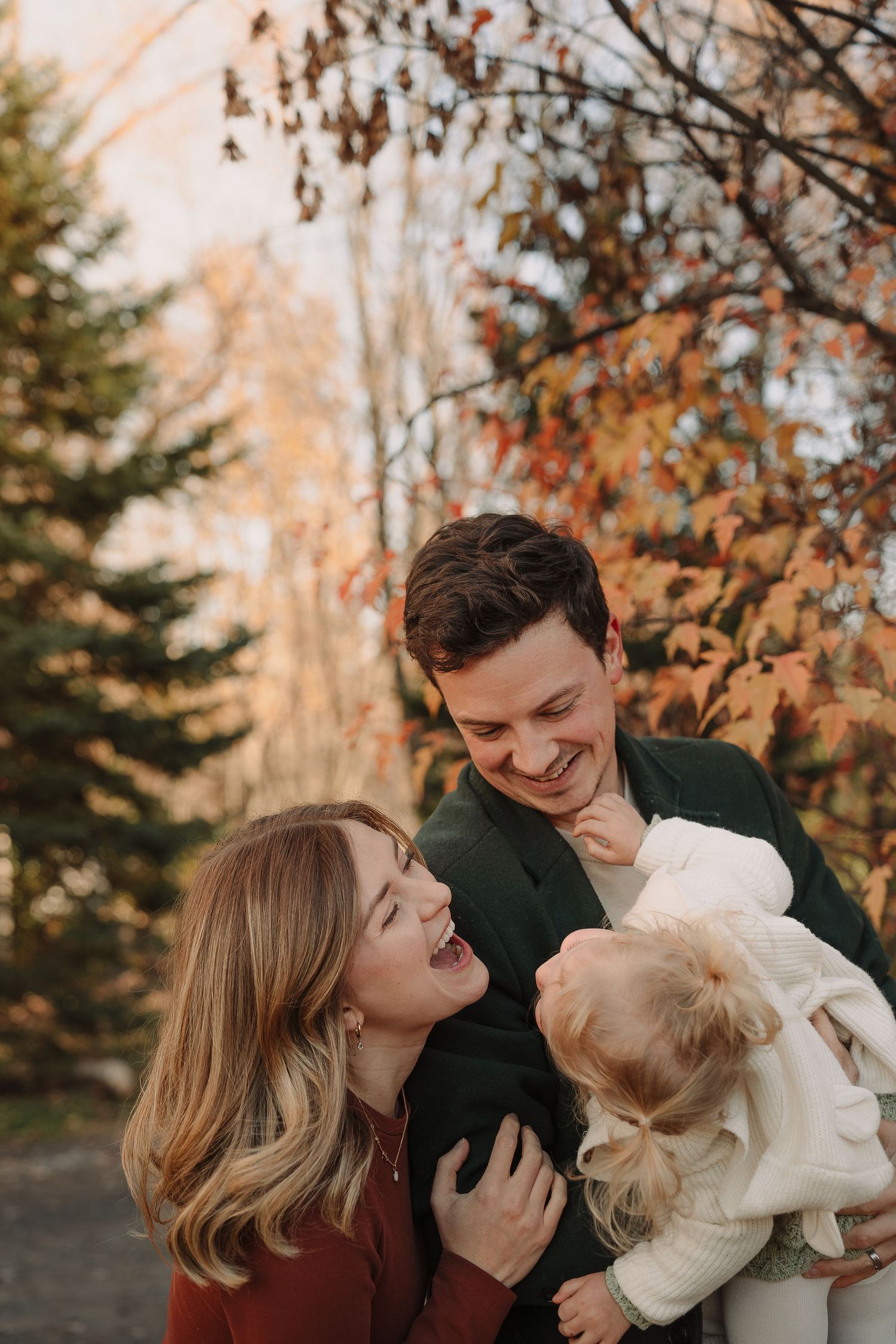 Family sharing playful moments together in a fall setting with golden light filtering through trees.
