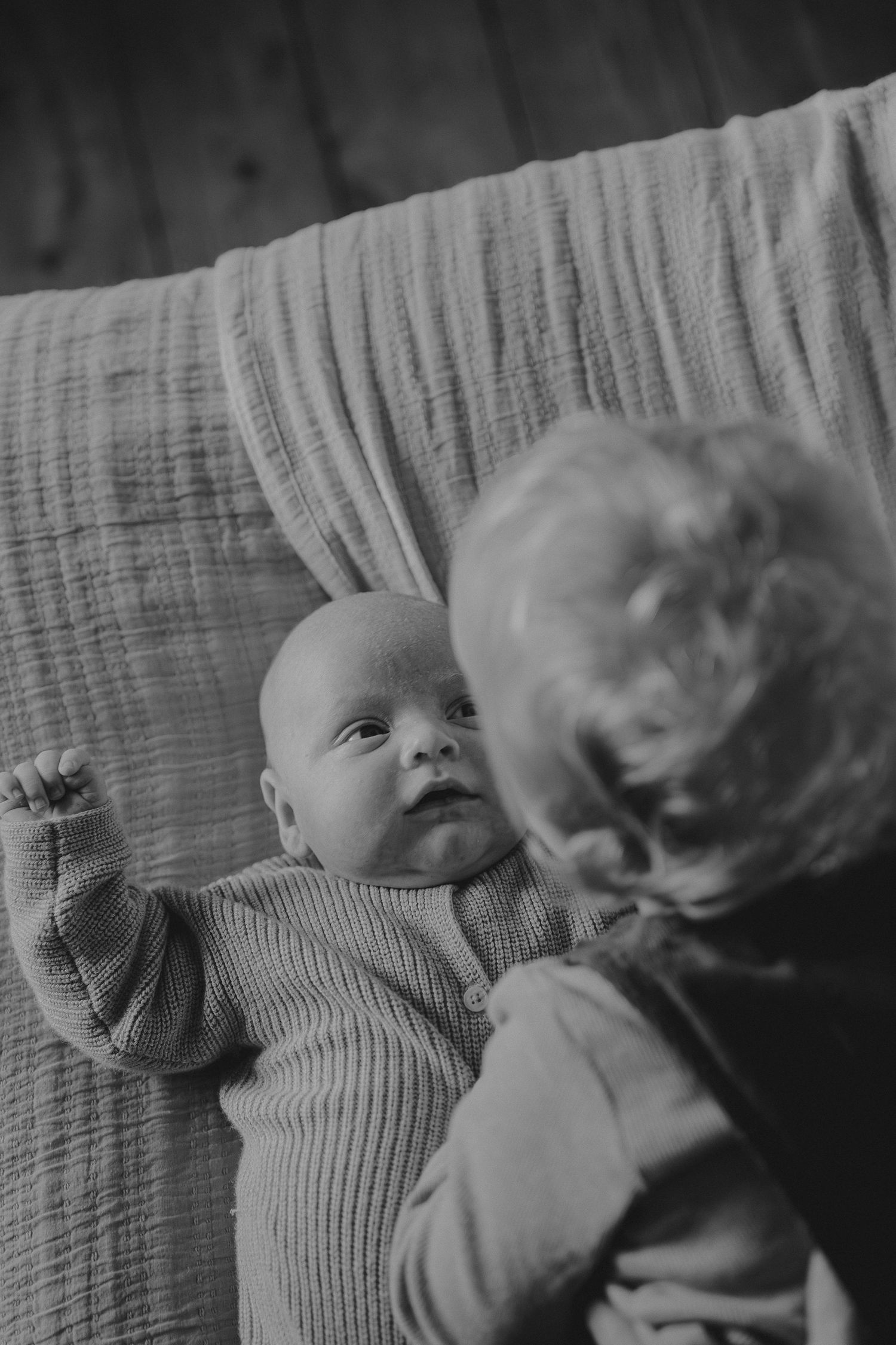 A baby wearing a ribbed sweater resting on textured fabric in black and white.