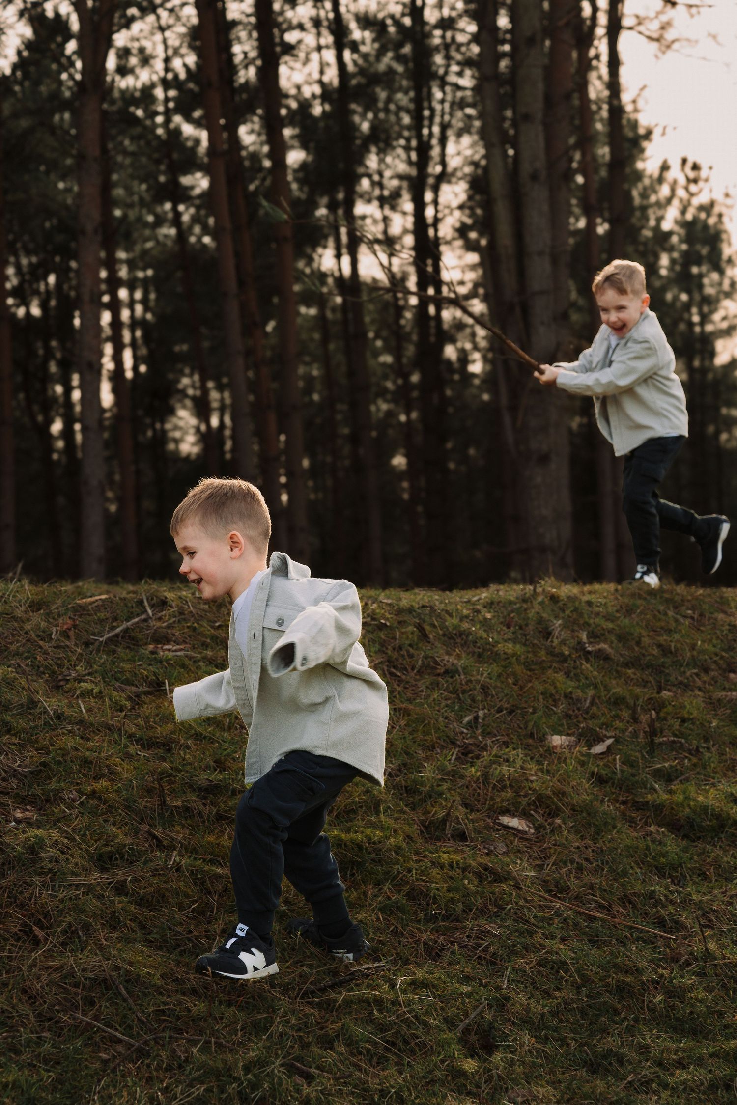 Child in white shirt playing and running down a forest hill at sunset.