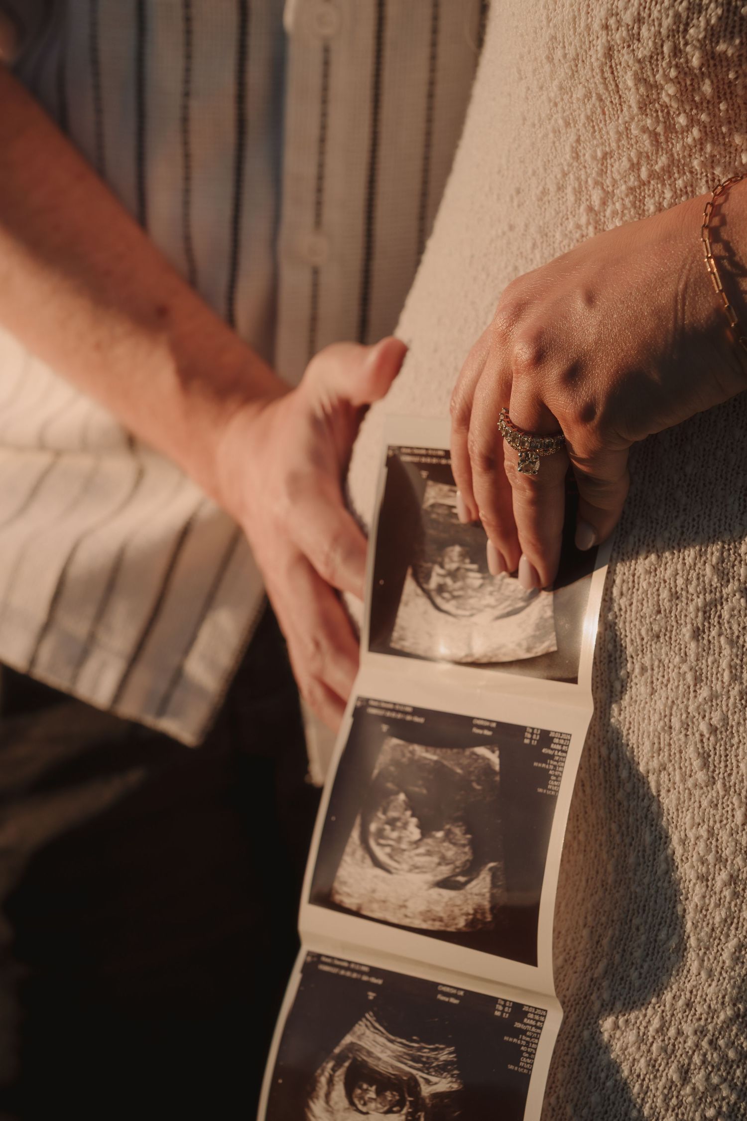 Couple holding ultrasound sonogram photos together, announcing pregnancy with warm golden light.