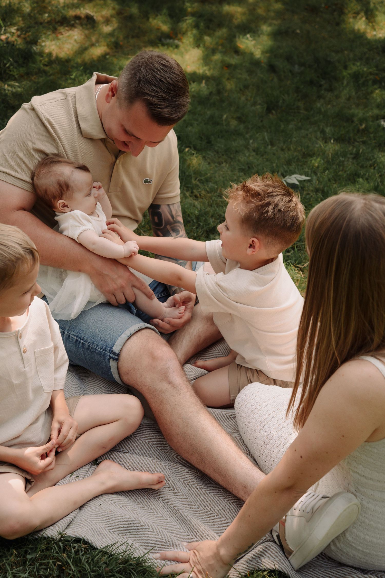 Family sitting together on a blanket outdoors during a casual summer photoshoot in a park.