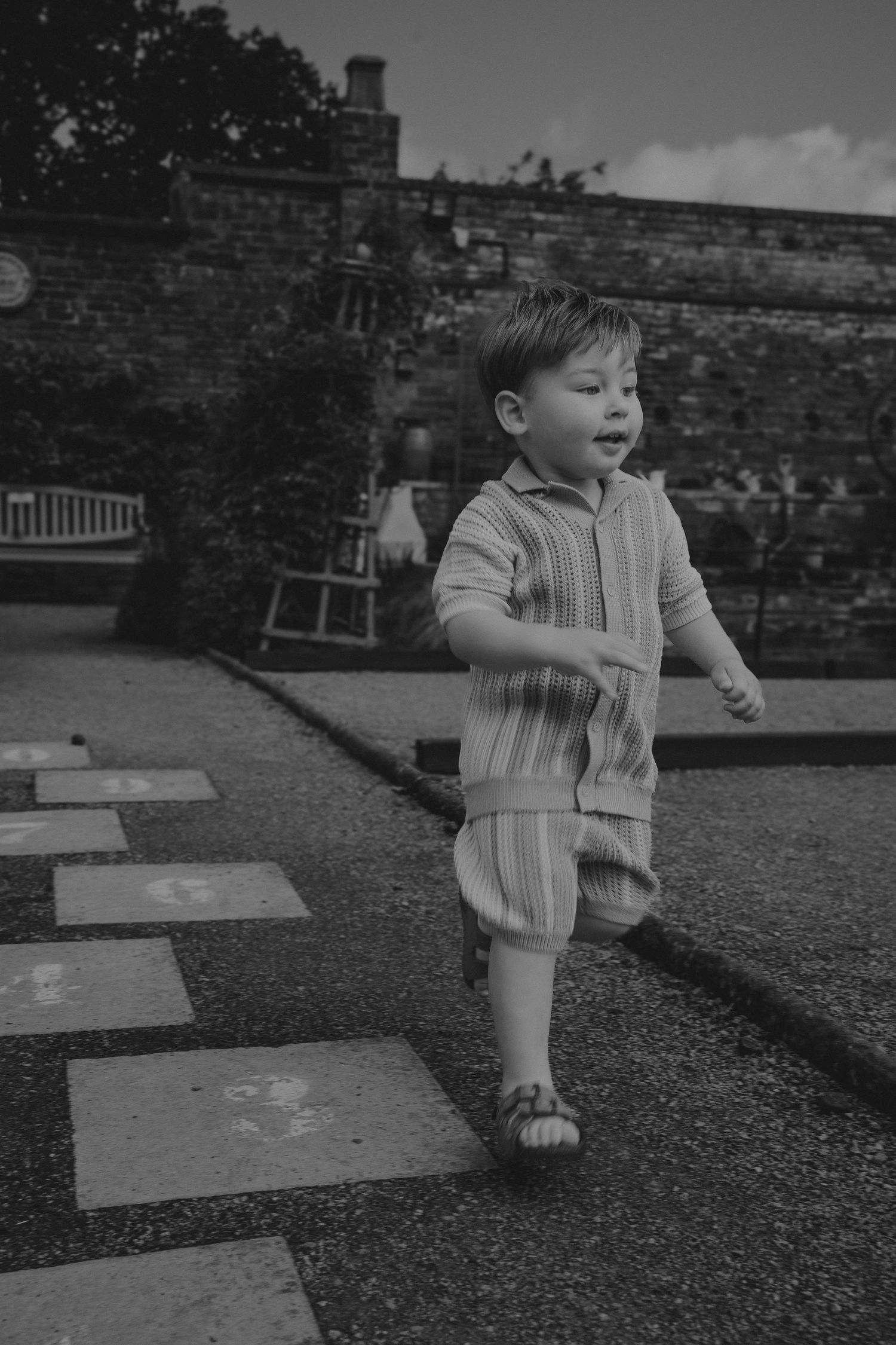 Black and white photo series of a toddler playing and running on a gravel path in a garden setting by a Tamworth family photographer.