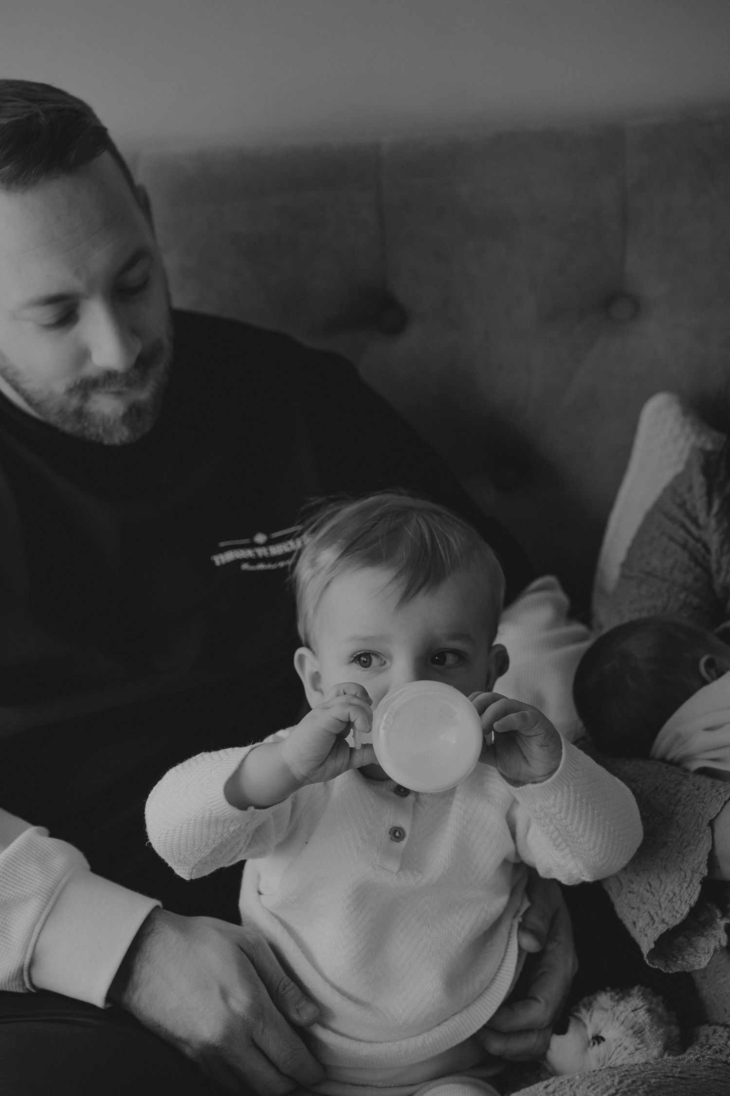 Black and white photo of a bearded father holding a toddler drinking from a sippy cup.