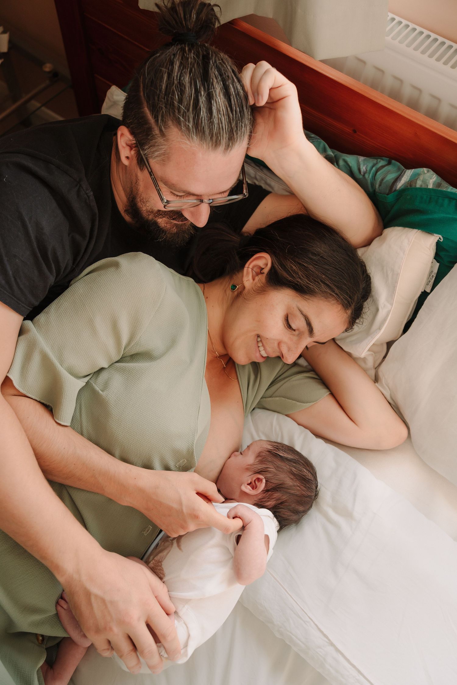 A tender family moment as parents cuddle with their newborn baby while resting together on a bed.