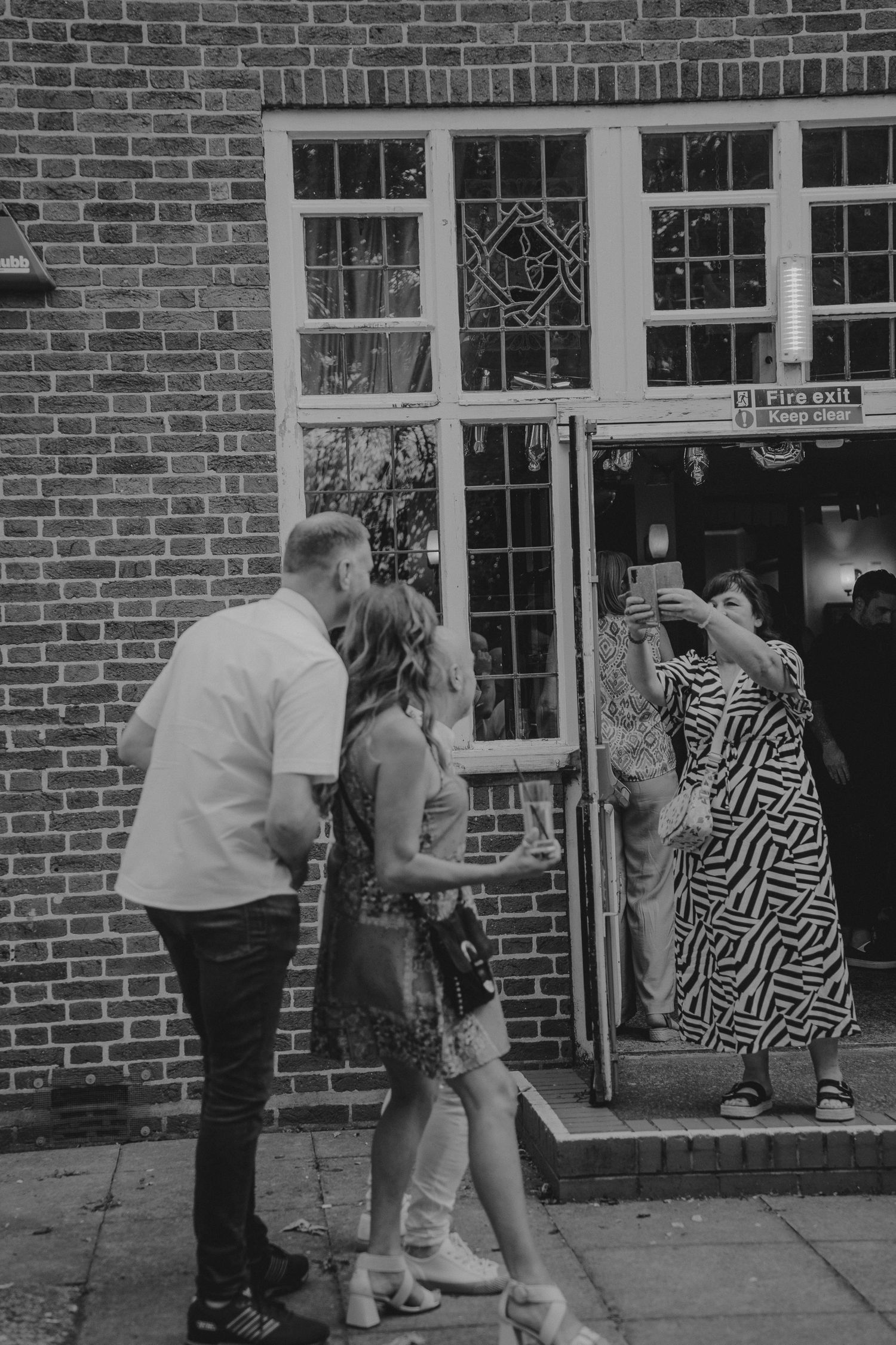 People dancing and interacting outside a brick building with windows.