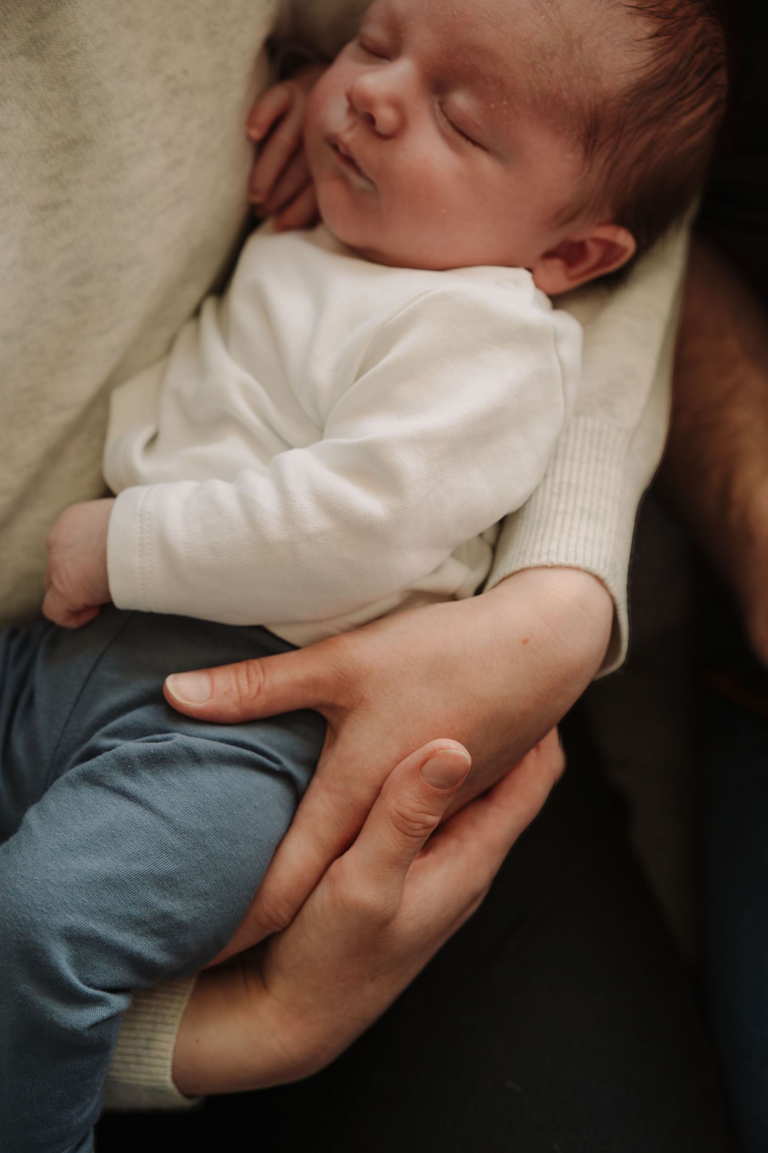 Sleeping baby being cuddled in their mum's arms during an at home session by Tamworth newborn photographer.