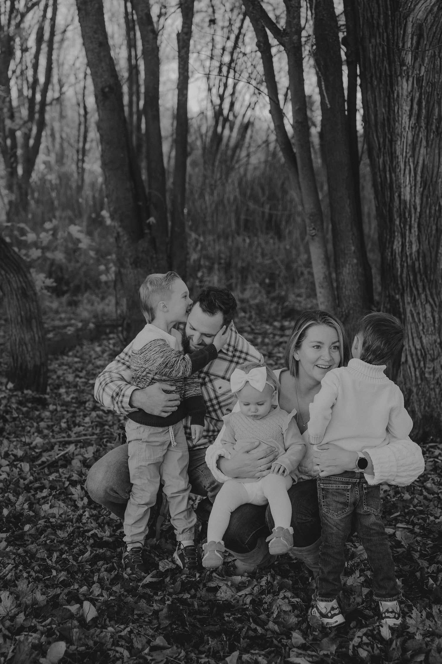 A vintage black and white photo show family playing and interacting on fallen leaves in a wooded area By a Tamworth family photographer.