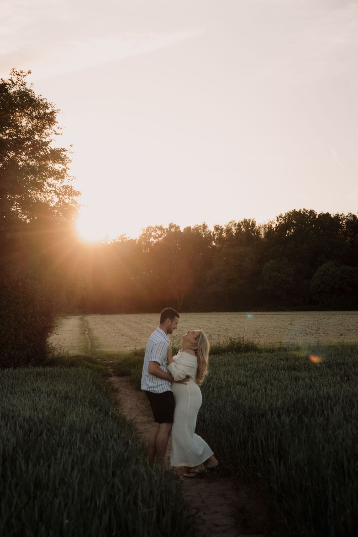 Couple embracing in a green field at golden sunset with trees in the background.