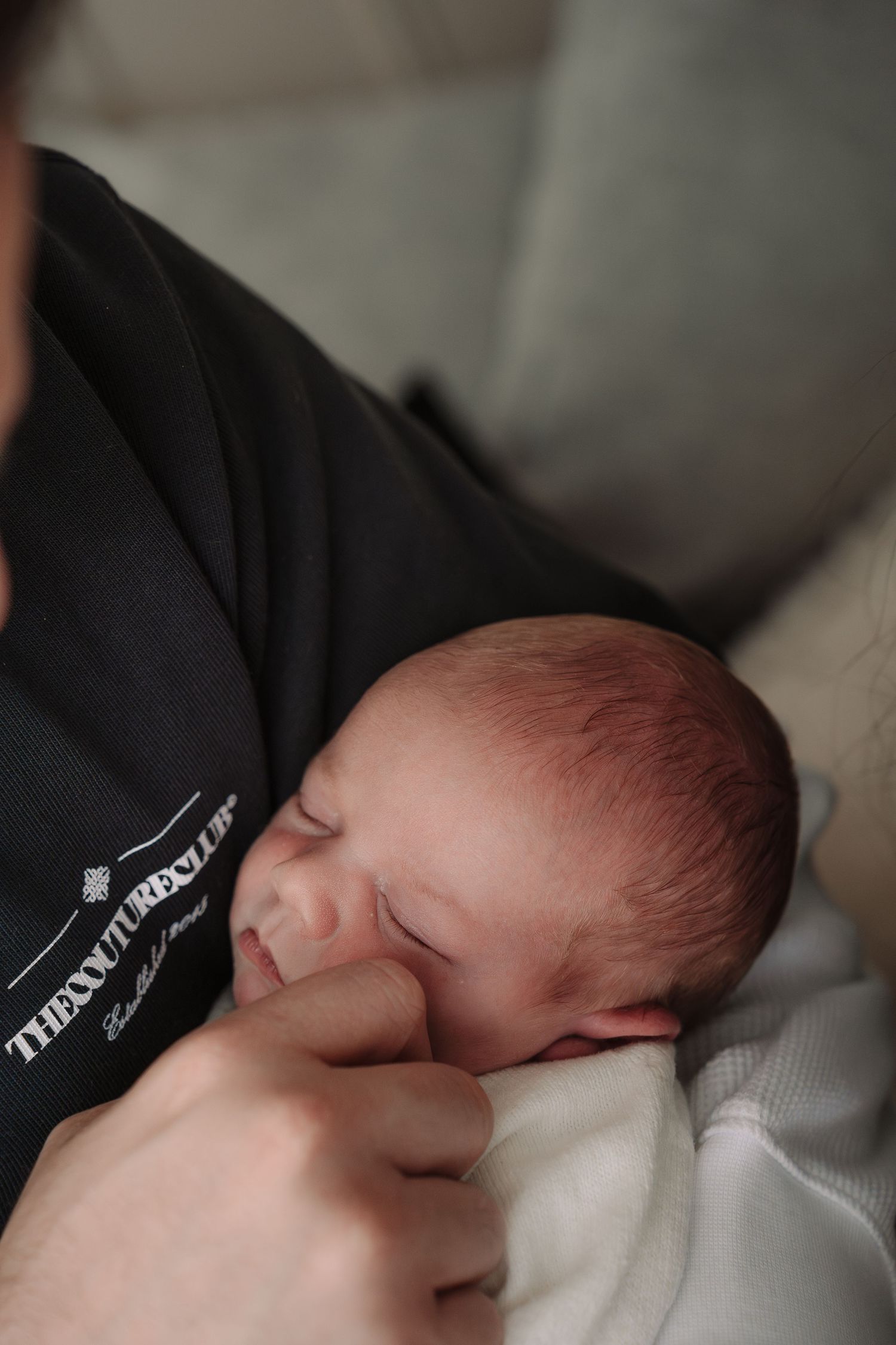 Newborn baby sleeping peacefully while being cradled in an adult's arms wearing a black shirt.