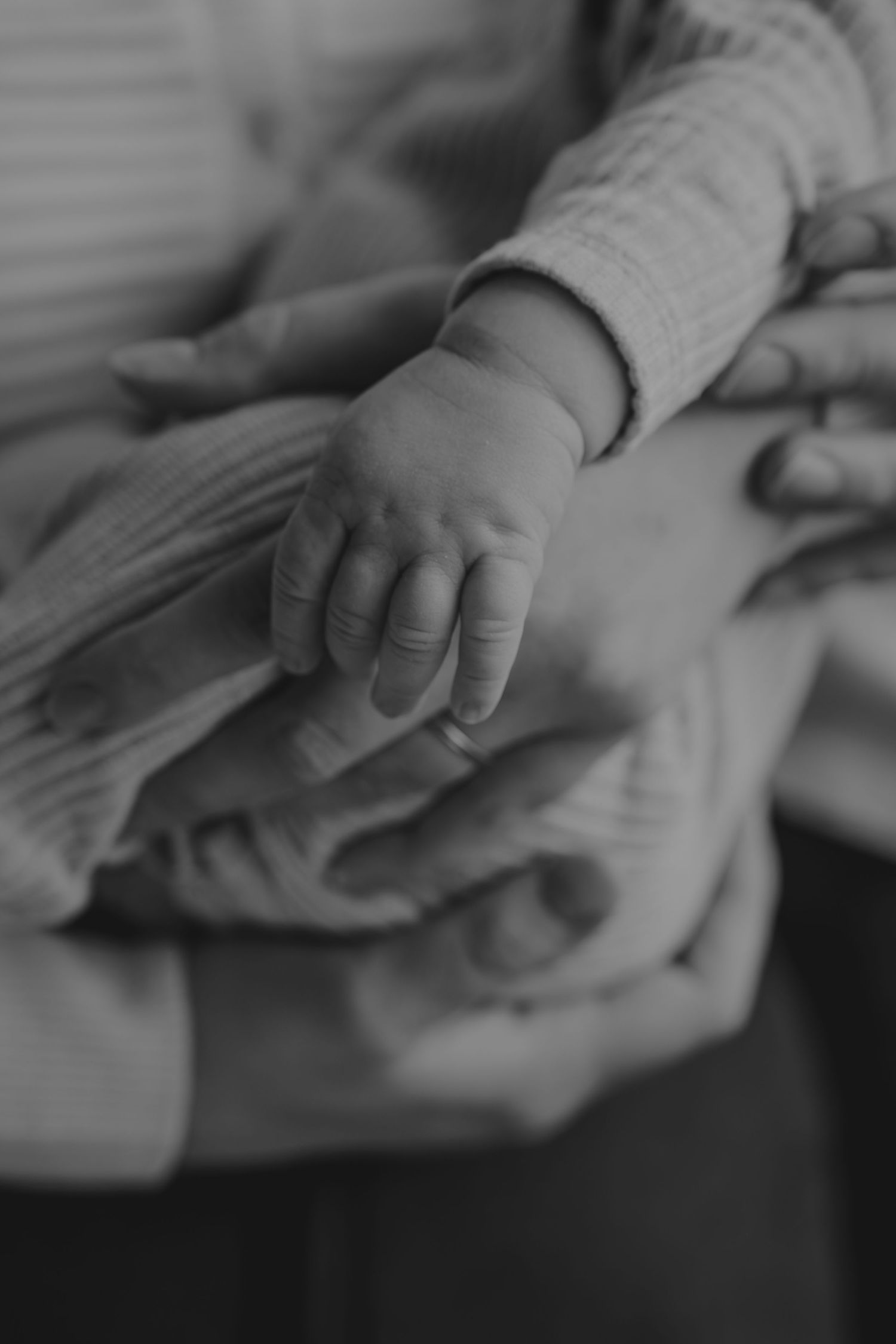 A close-up black and white photo shows a small baby's hand gently resting on a soft blanket.