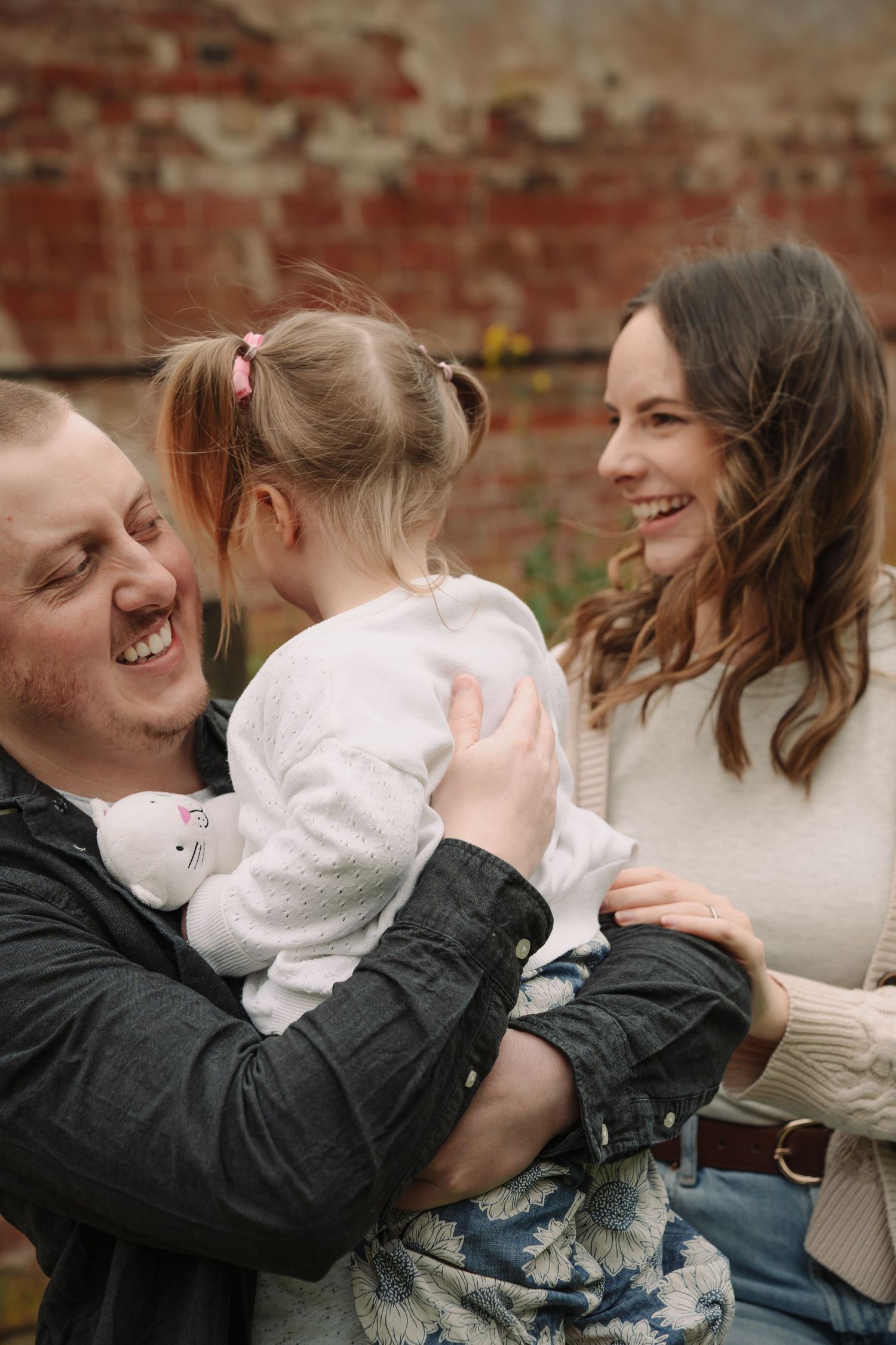 A family shares a joyful moment together outdoors against a rustic brick wall background.
