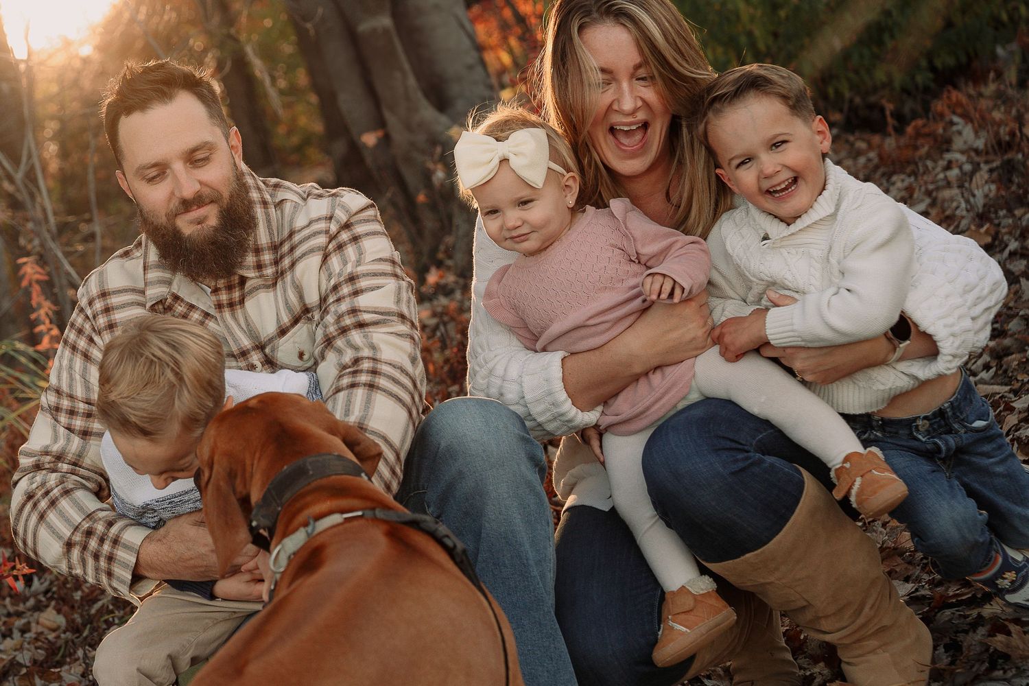 A happy family with children and dog sitting together on autumn leaves during an outdoor photo session by Tamworth family photographer.