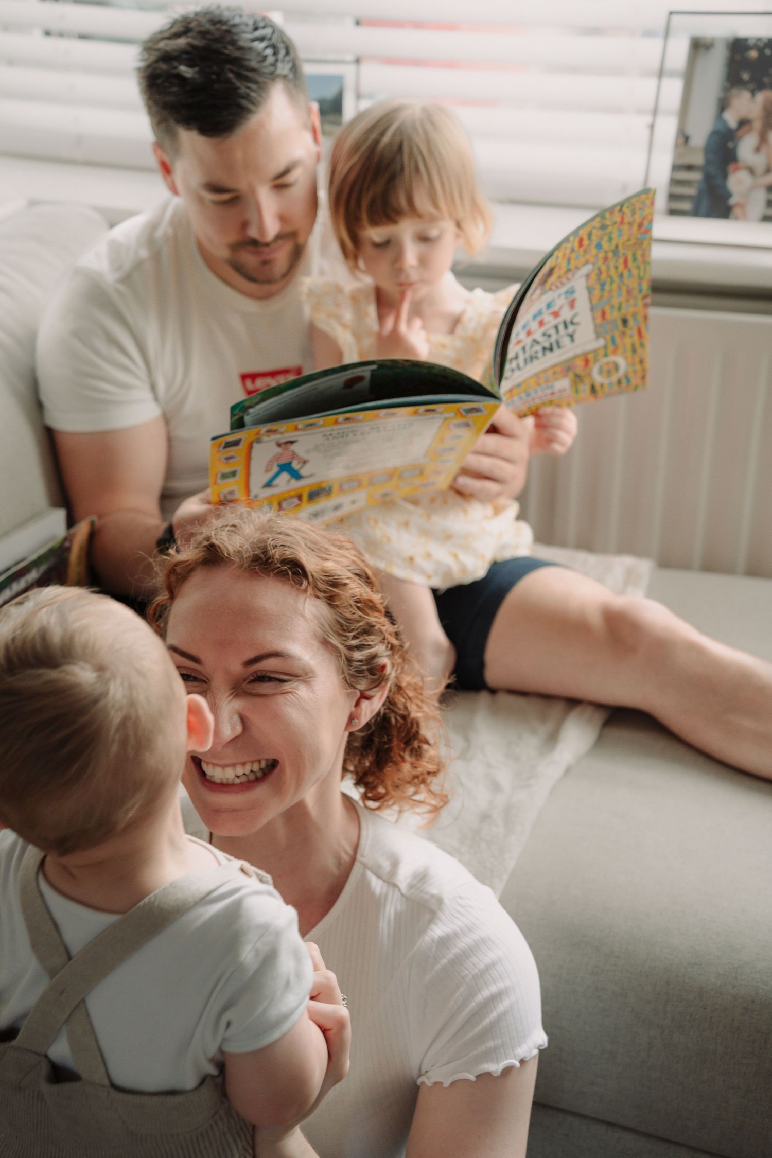 Dad and girl reading a book in the background while mum and little boy are laughing each other in the foreground by Tamworth photographer.